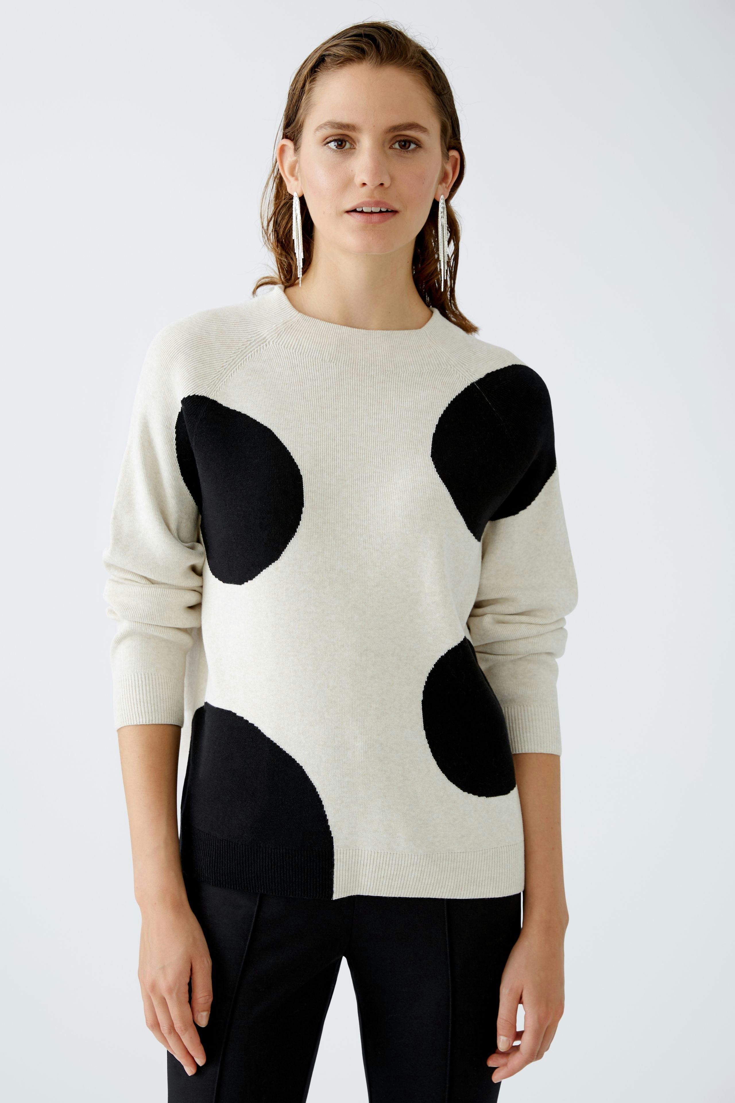 Modern pullover: Woman in a light sweater with black polka dots, paired with sleek black pants.