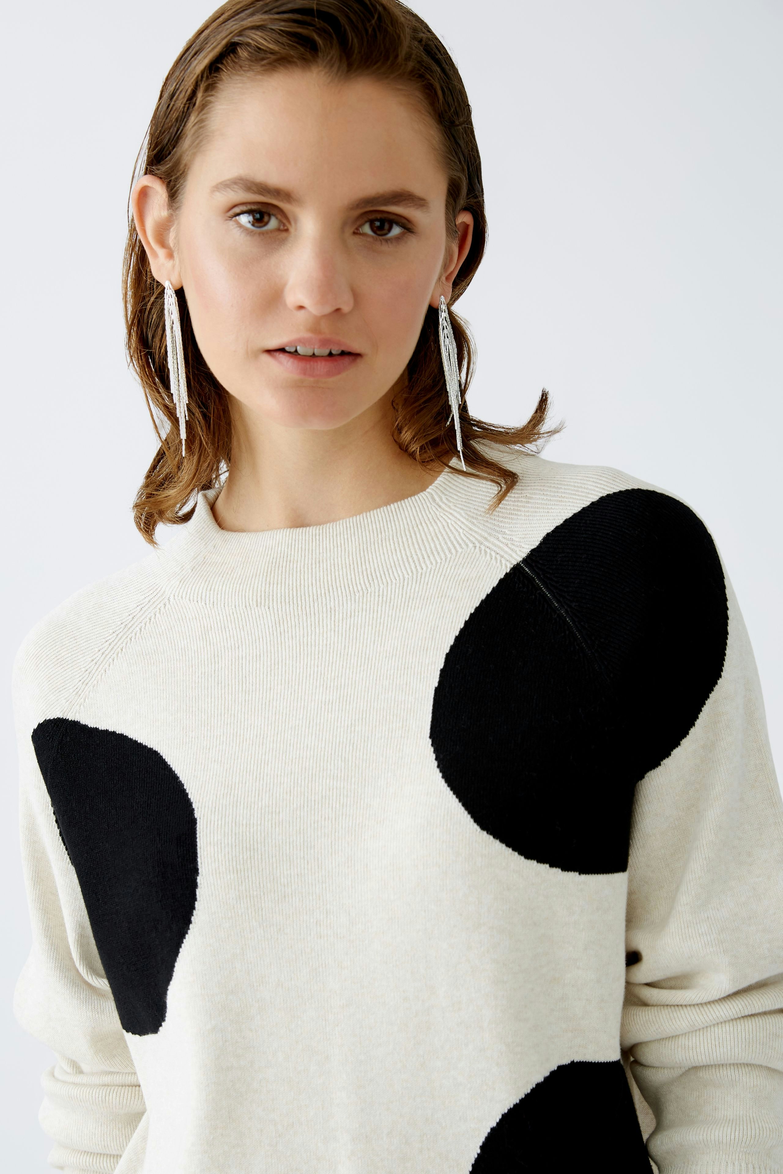 Modern women's pullover: A woman in a cream pullover with black spots, exuding casual elegance.