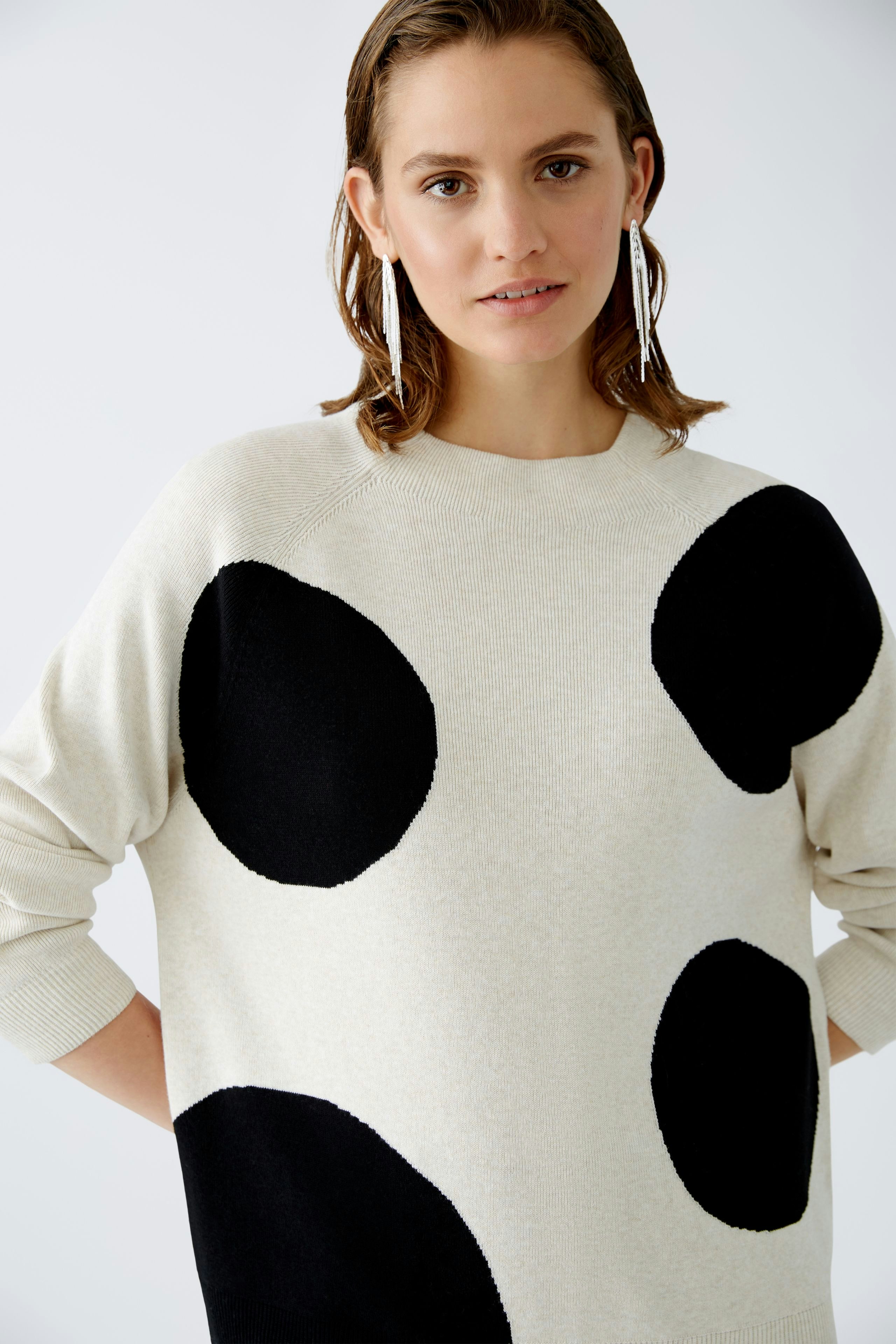 Stylish women's pullover: A woman in a cream pullover with bold black dots, exuding modern elegance.