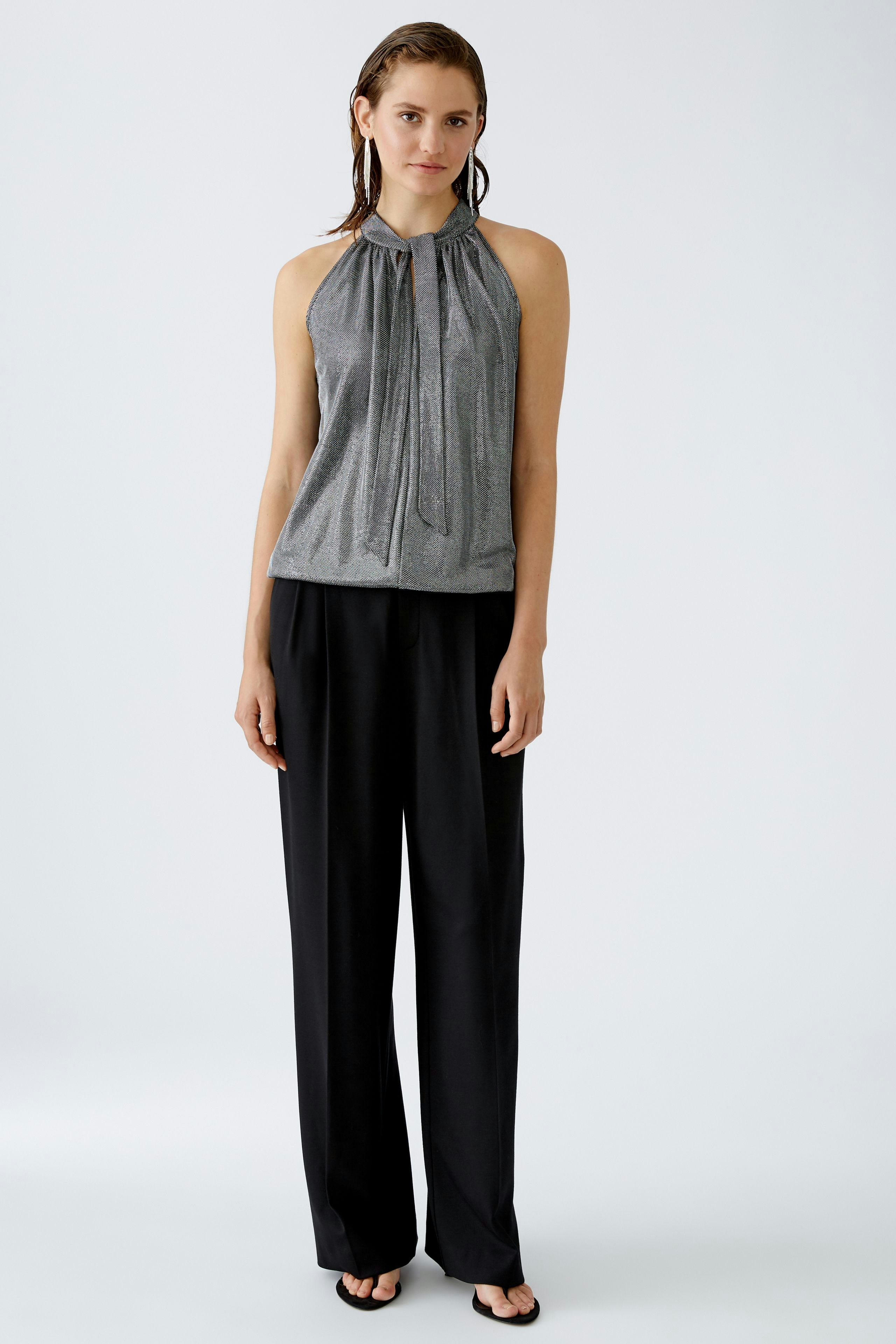 Elegantes Damen-Top: Frau in schimmerndem, grauem Top mit lässiger Hose steht selbstbewusst.