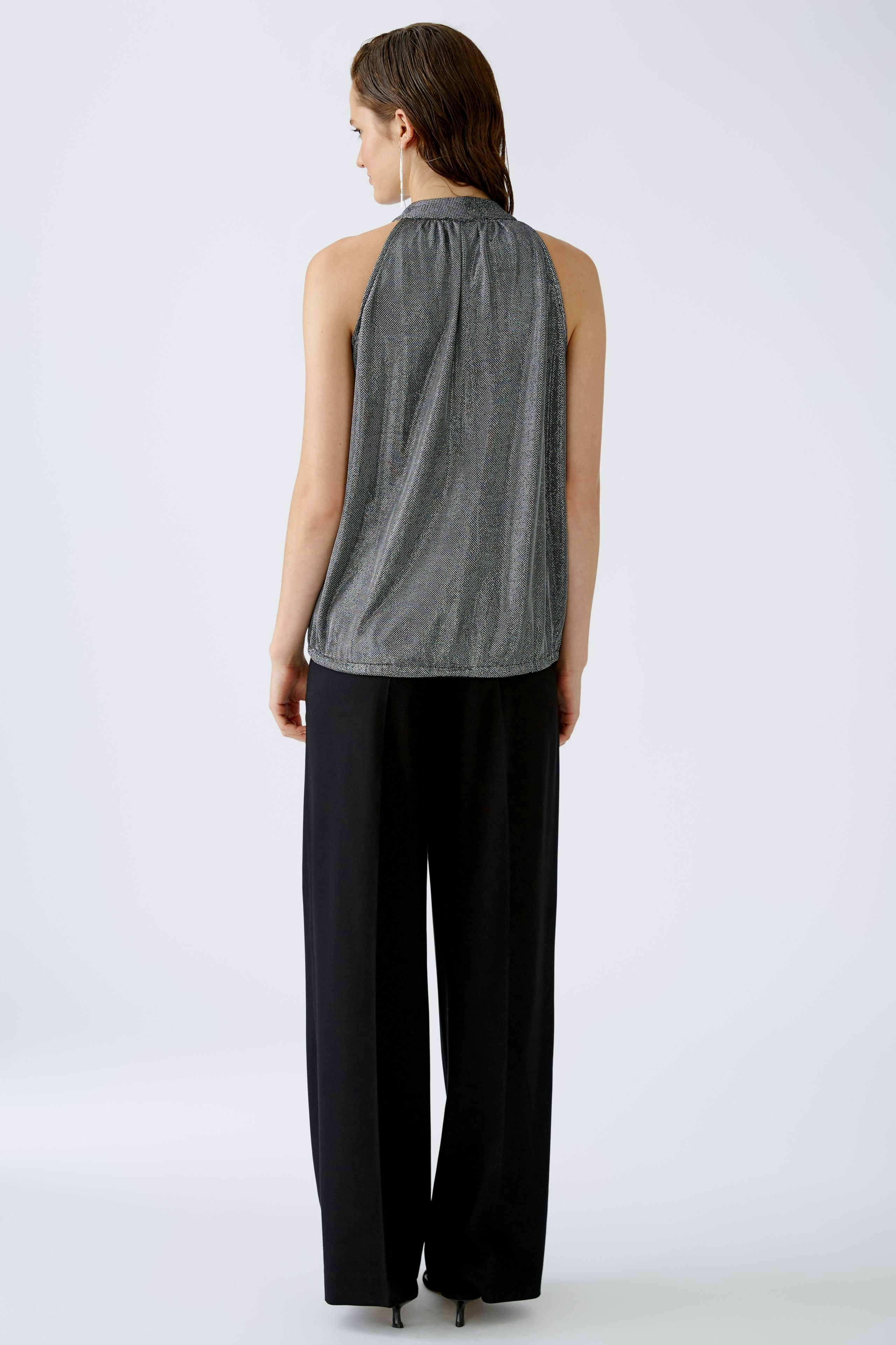 Elegantes Damen-Top: Frau in schimmerndem, ärmellosem Top mit lässiger Hose von hinten.