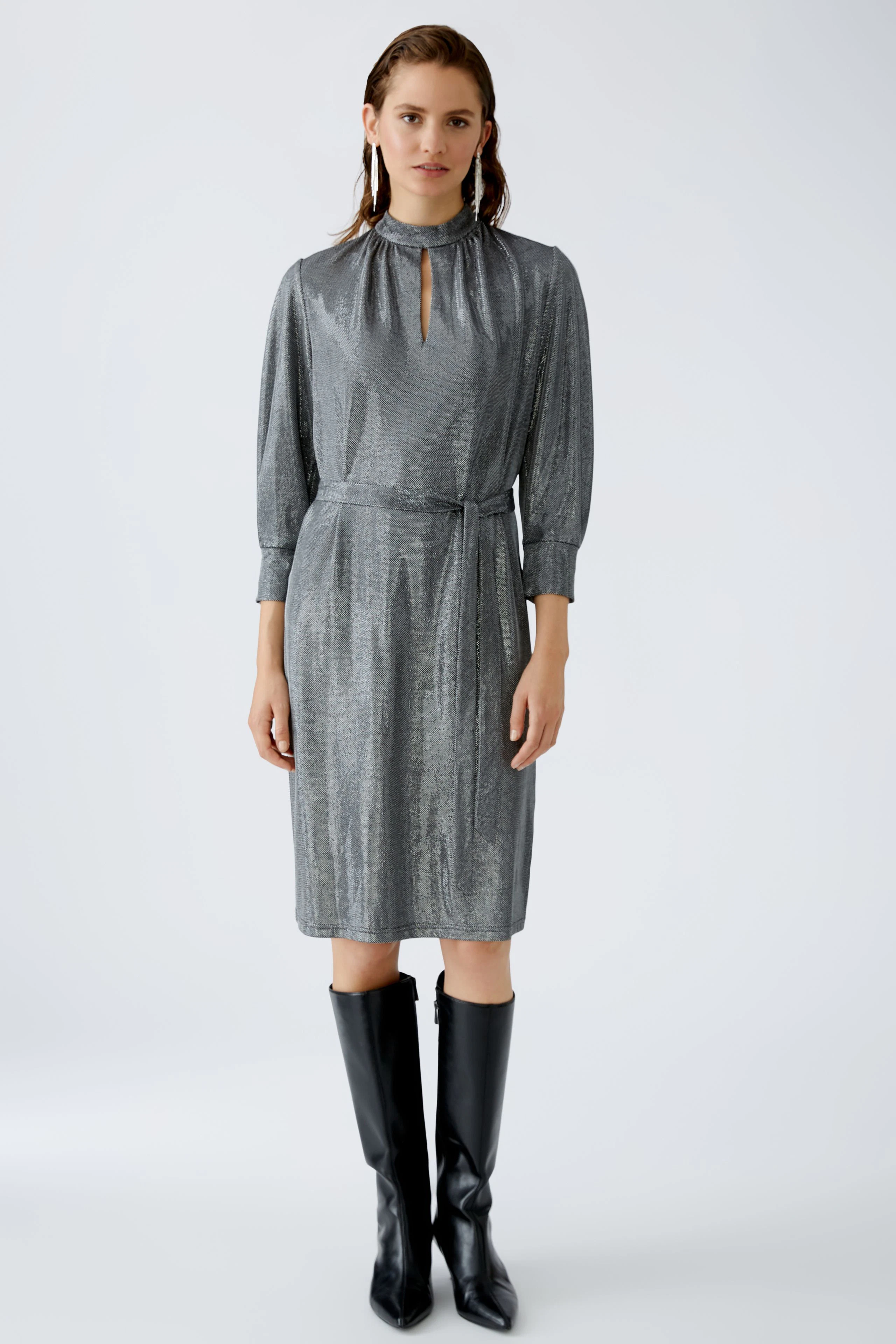 Elegantes Abendkleid: Frau in schimmerndem, grauem Kleid mit Stehkragen und Gürtel.