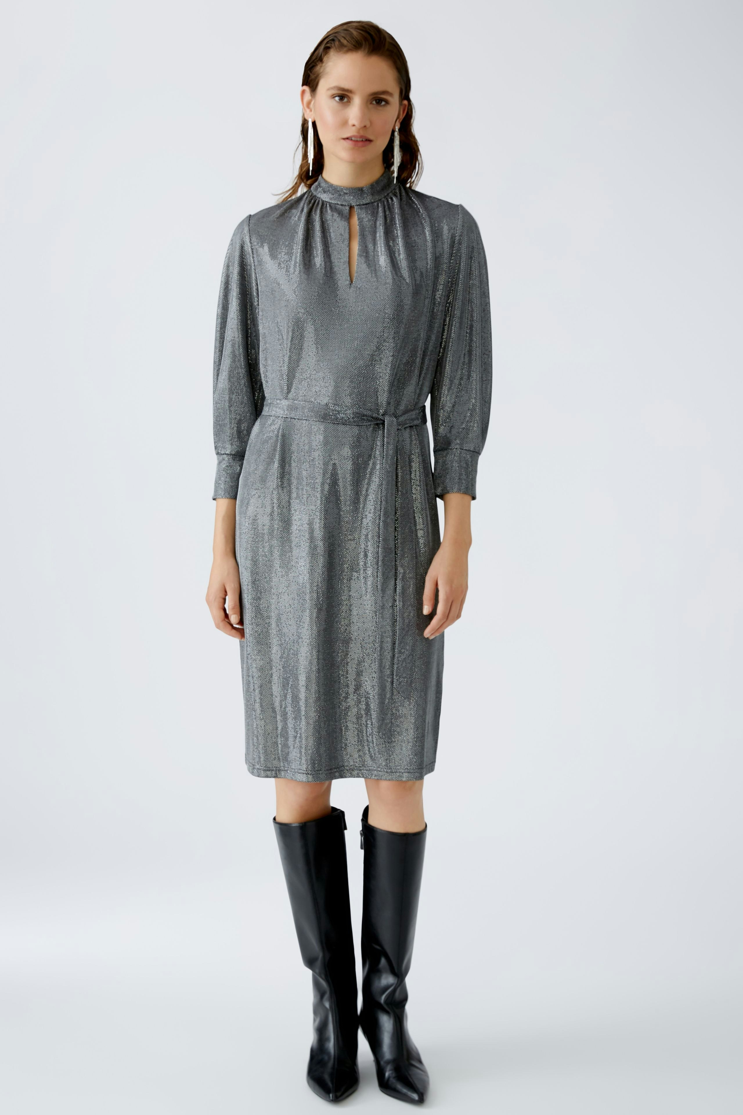 Elegantes Abendkleid: Frau in schimmerndem, grauem Kleid mit Stehkragen und Gürtel.