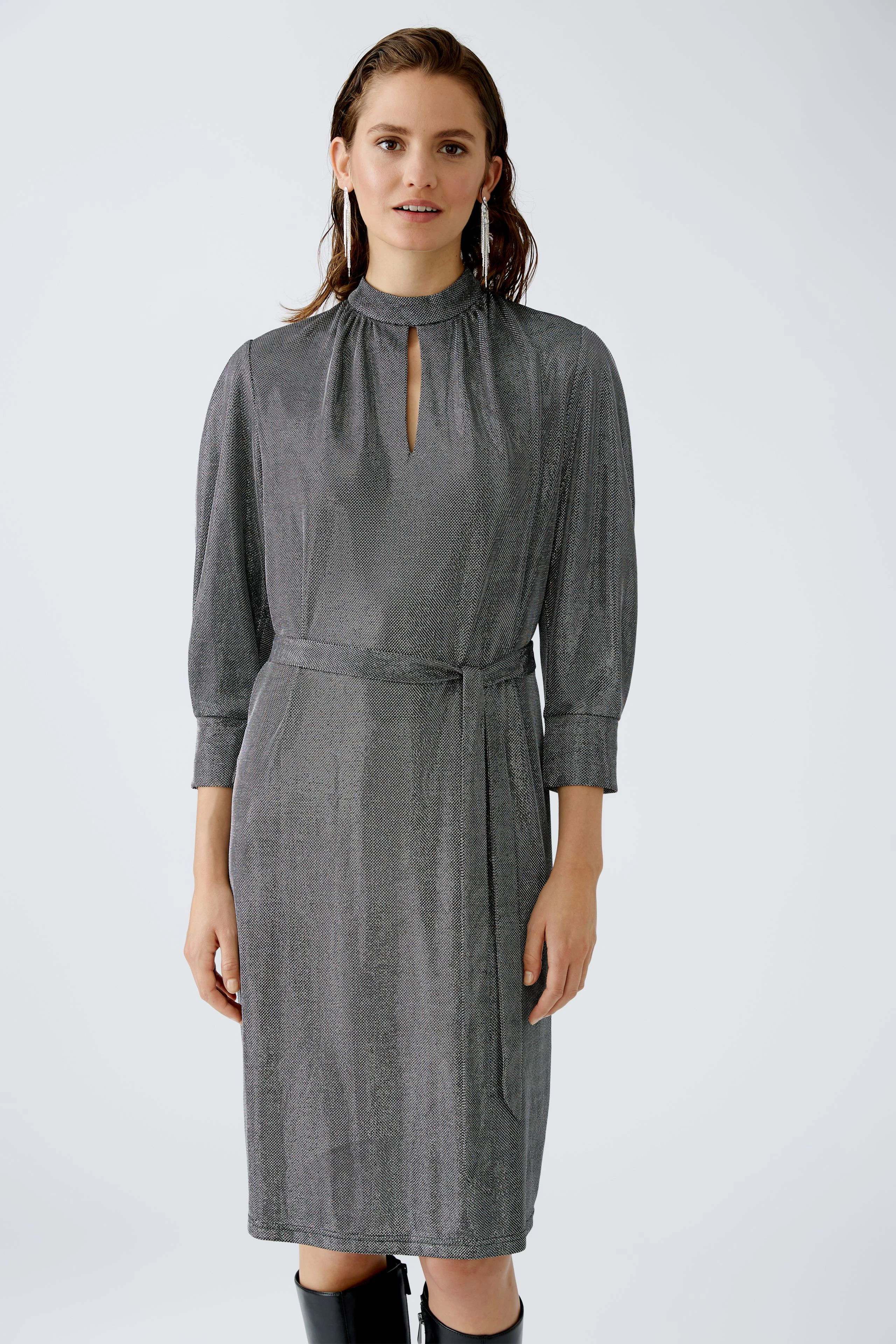 Elegantes Abendkleid: Frau in schimmerndem, grauem Kleid mit Stehkragen und Taillengürtel.