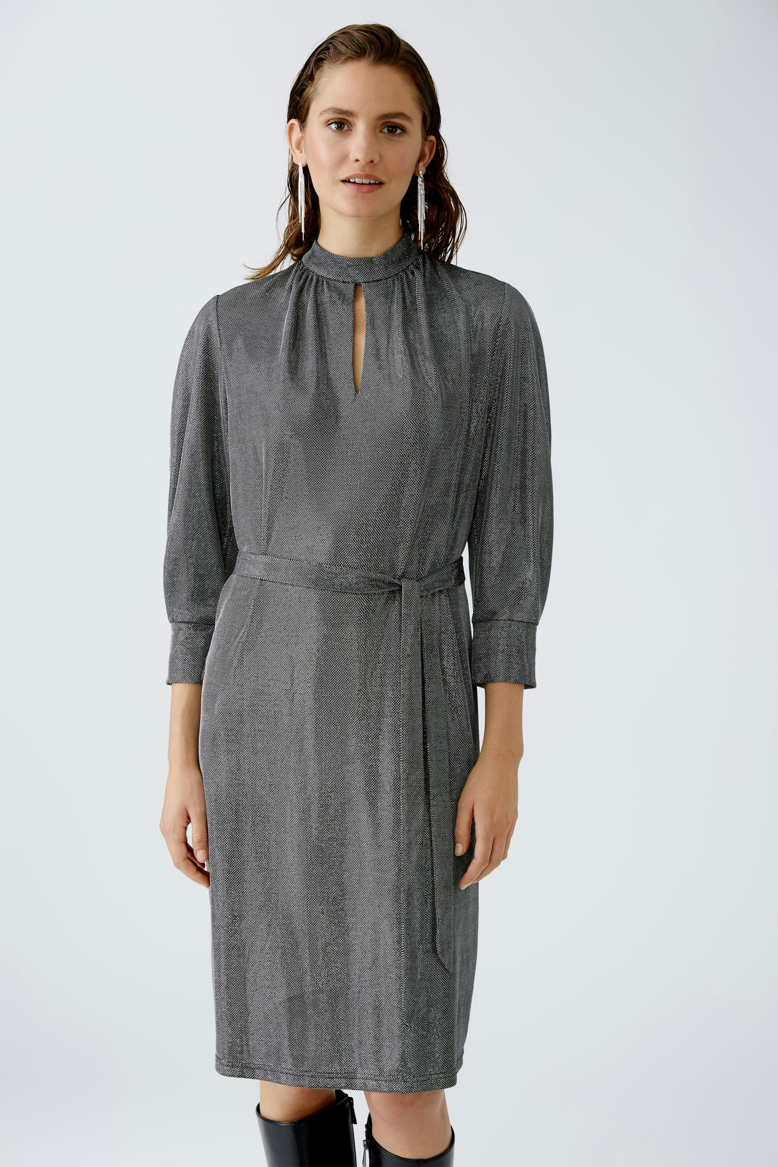 Elegantes Abendkleid: Frau in schimmerndem, grauem Kleid mit Stehkragen und Taillengürtel.