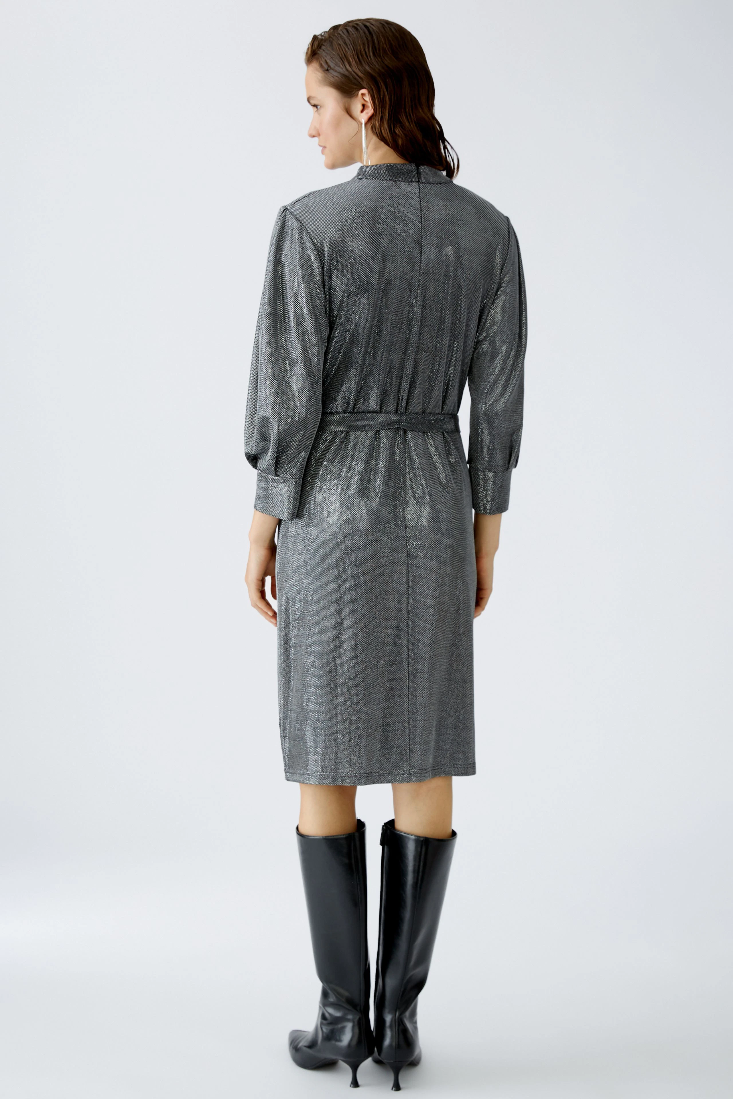 Elegantes Abendkleid: Frau in schimmerndem, grauem Kleid mit langen Ärmeln und Gürtel.