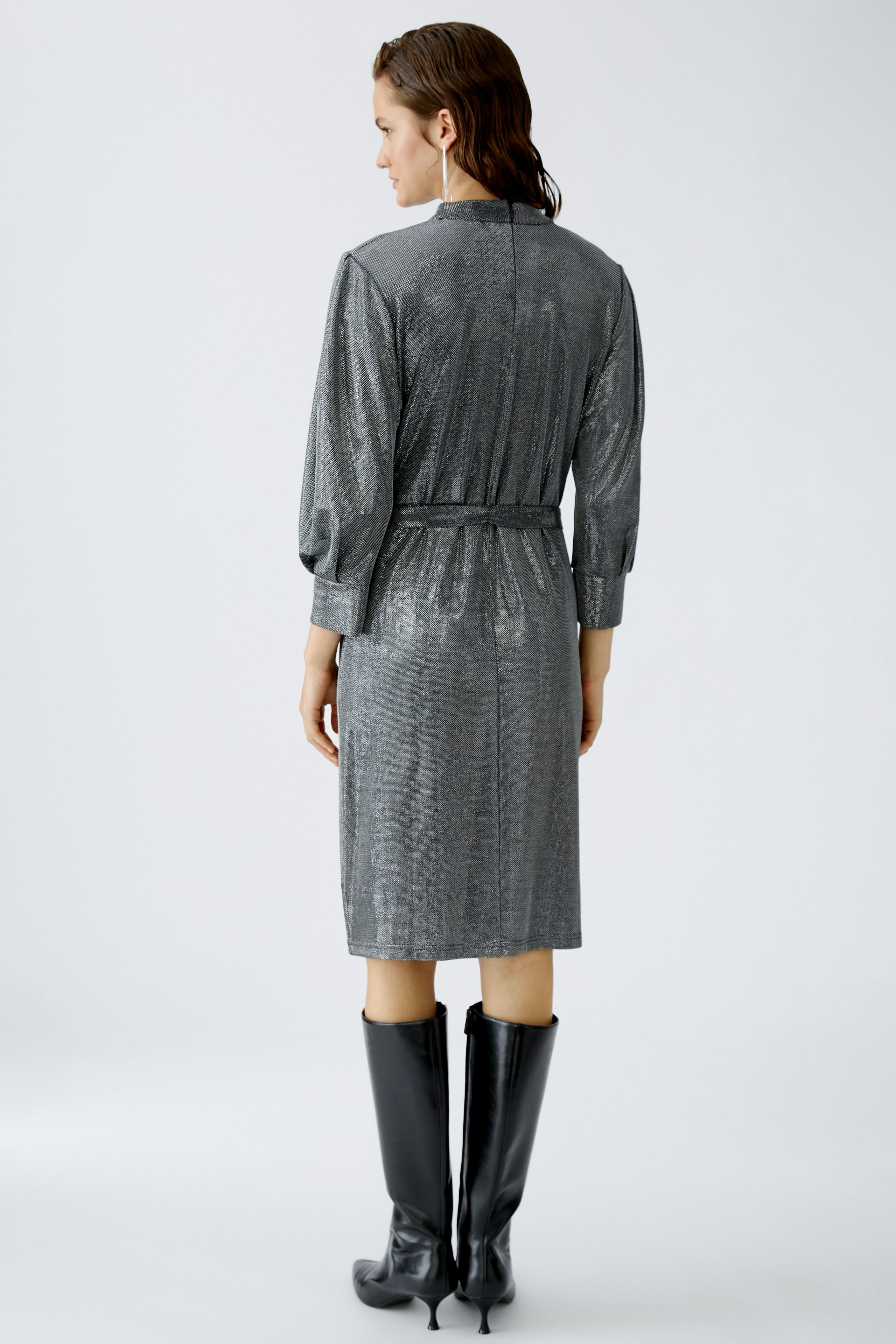 Elegantes Abendkleid: Frau in schimmerndem, grauem Kleid mit langen Ärmeln und Gürtel.