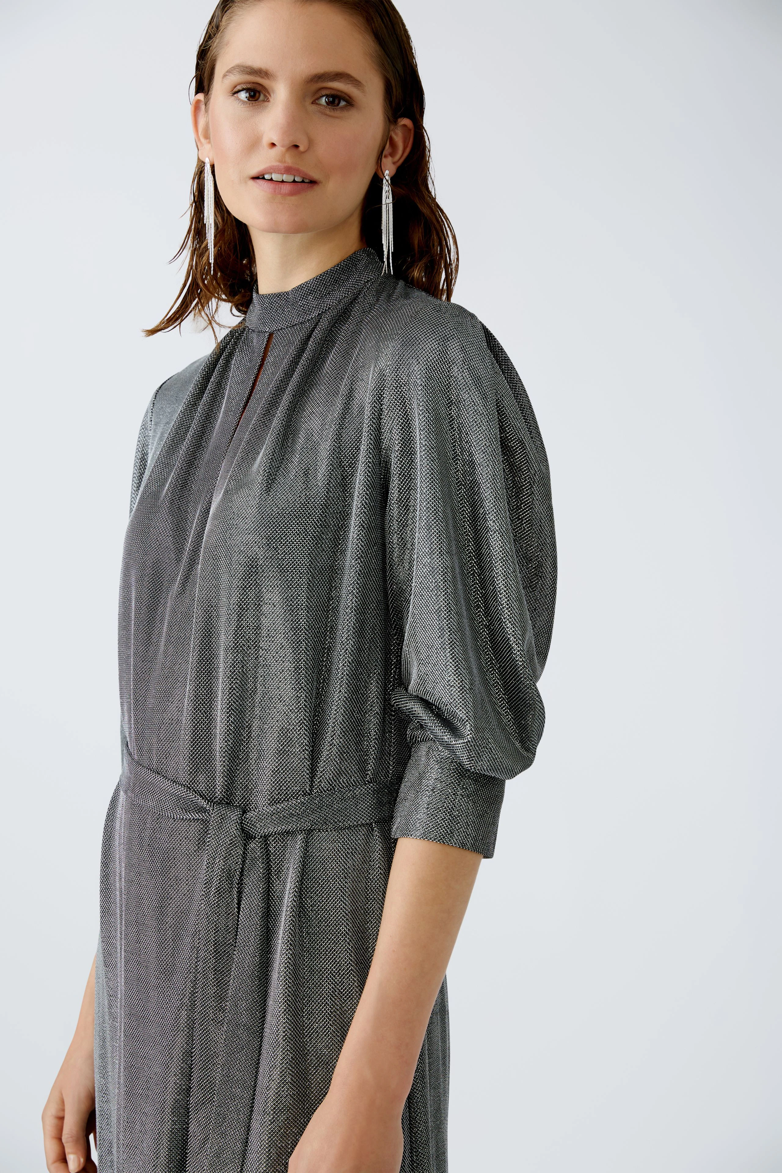 Elegantes Abendkleid: Frau in schimmerndem, grauem Kleid mit Stehkragen und lässigen Ärmeln.