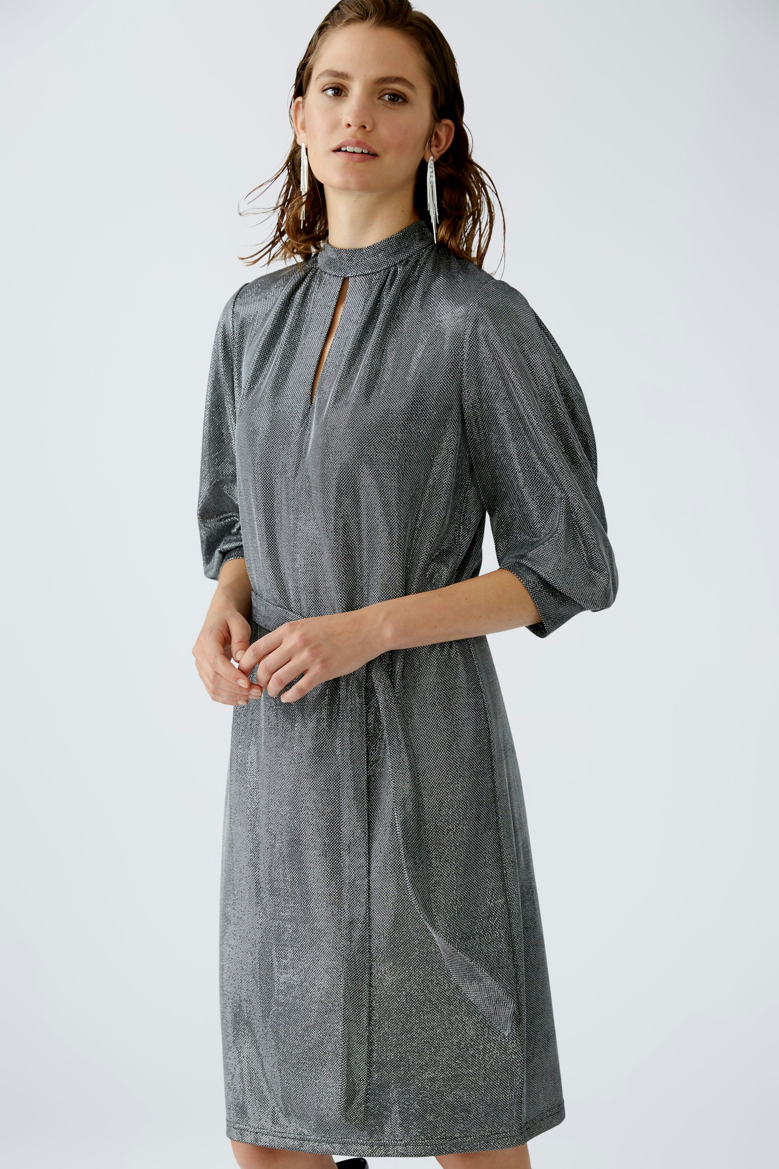 Elegantes Abendkleid: Frau in schimmerndem, grauem Kleid mit Stehkragen und lässigem Schnitt.