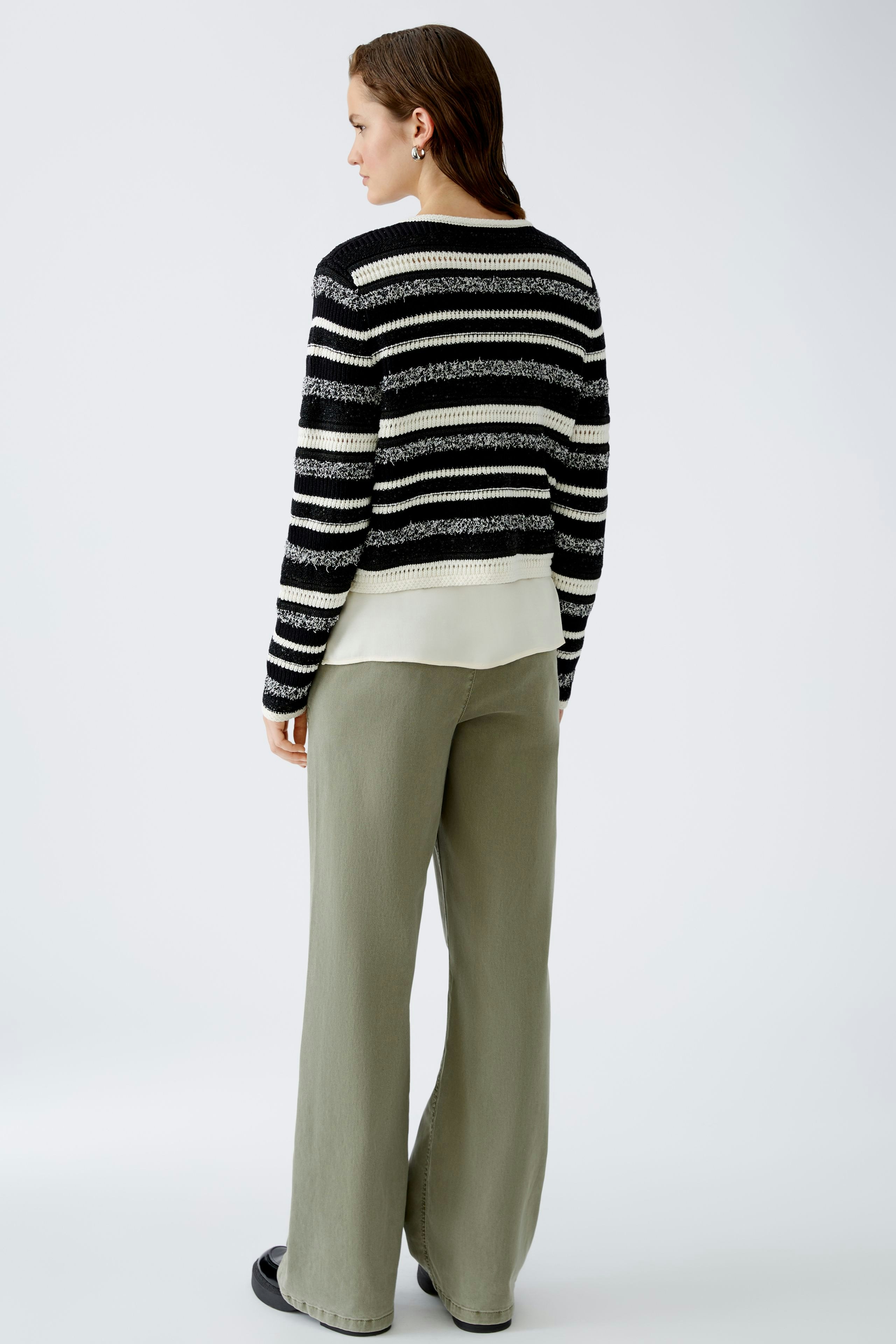 Damen-Strickjacke: Frau mit gestreifter Strickjacke in Schwarz und Weiß, lässig kombiniert mit weiten Hosen.