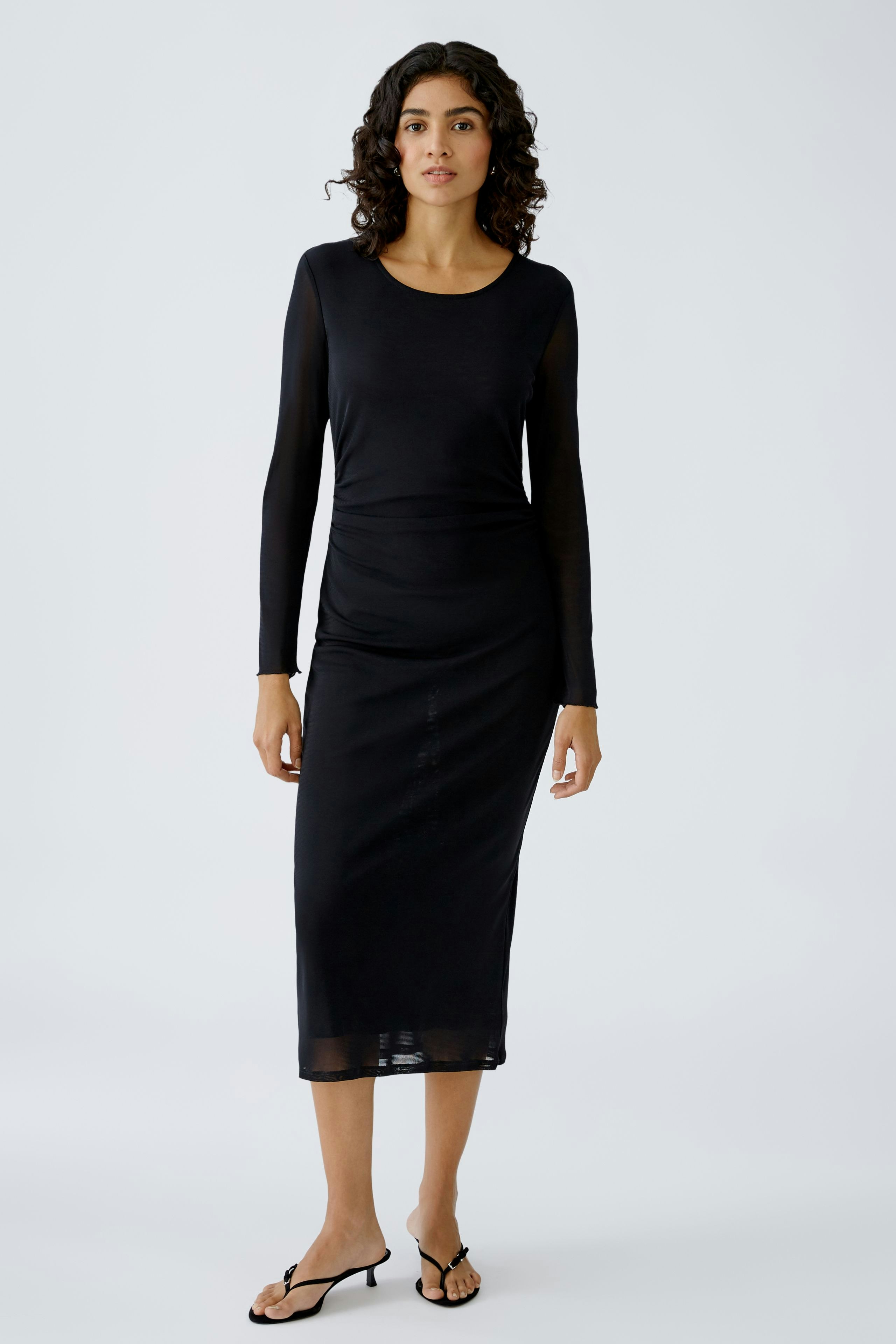 Elegant black midi dress: A woman in a fitted long-sleeve dress, showcasing a sleek silhouette.