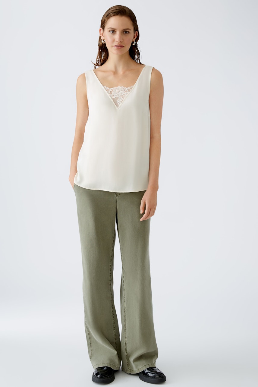 Elegant women's top with lace detail, paired with relaxed-fit trousers for a chic look.