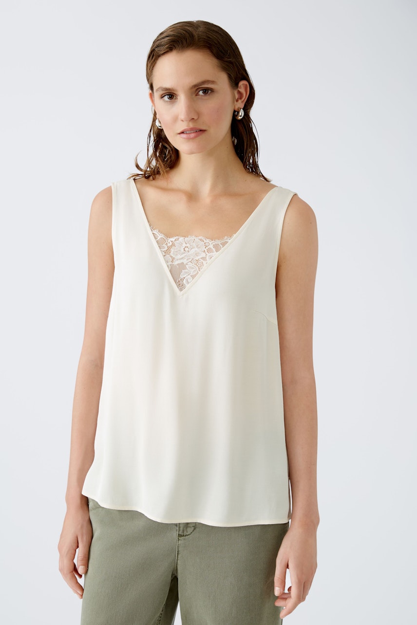 Elegant women's top: A woman in a light cream sleeveless top with lace detail, exuding effortless style.