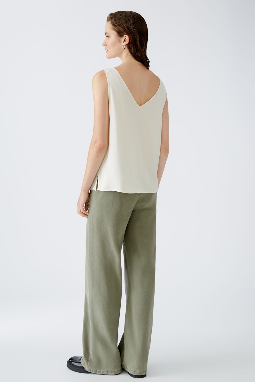 Elegant women's top: A woman in a cream sleeveless top with a V-back, paired with wide-leg trousers.