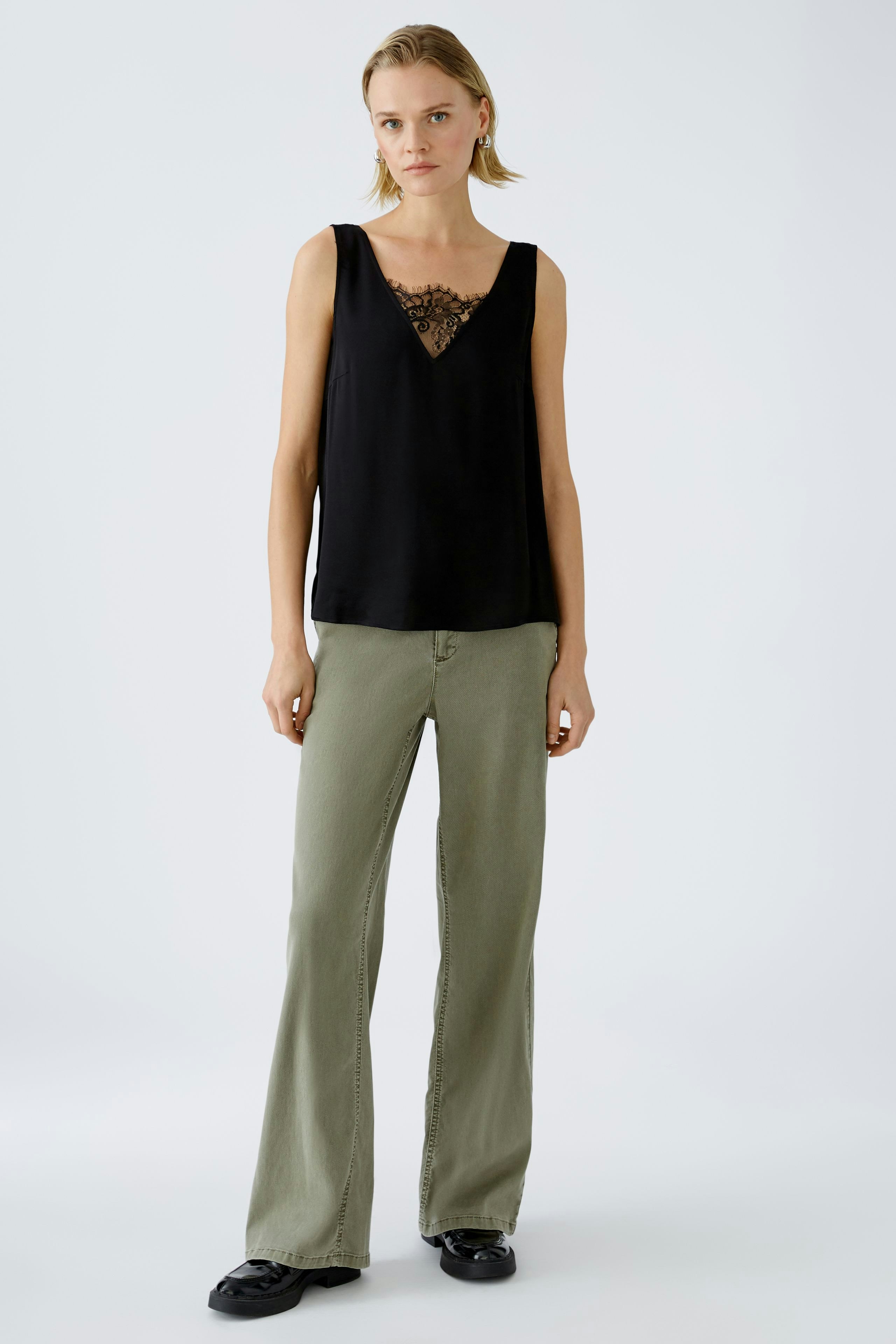 Elegant women's top: A woman in a black sleeveless top with lace detail, paired with relaxed-fit pants.