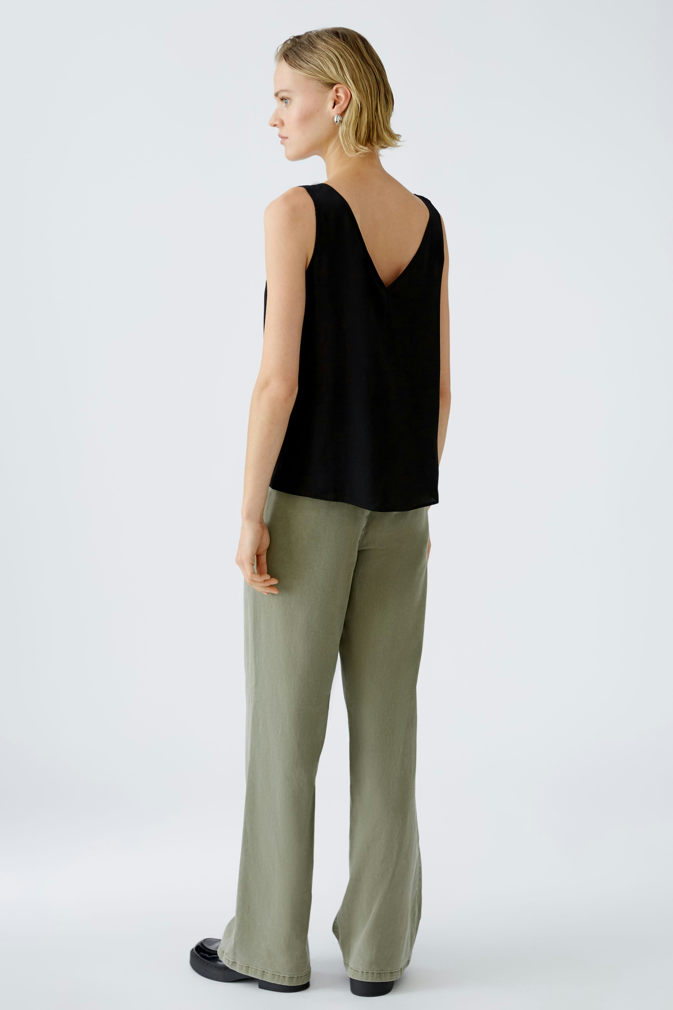Elegant women's top: A woman in a black sleeveless top with a V-neck, paired with light green trousers.