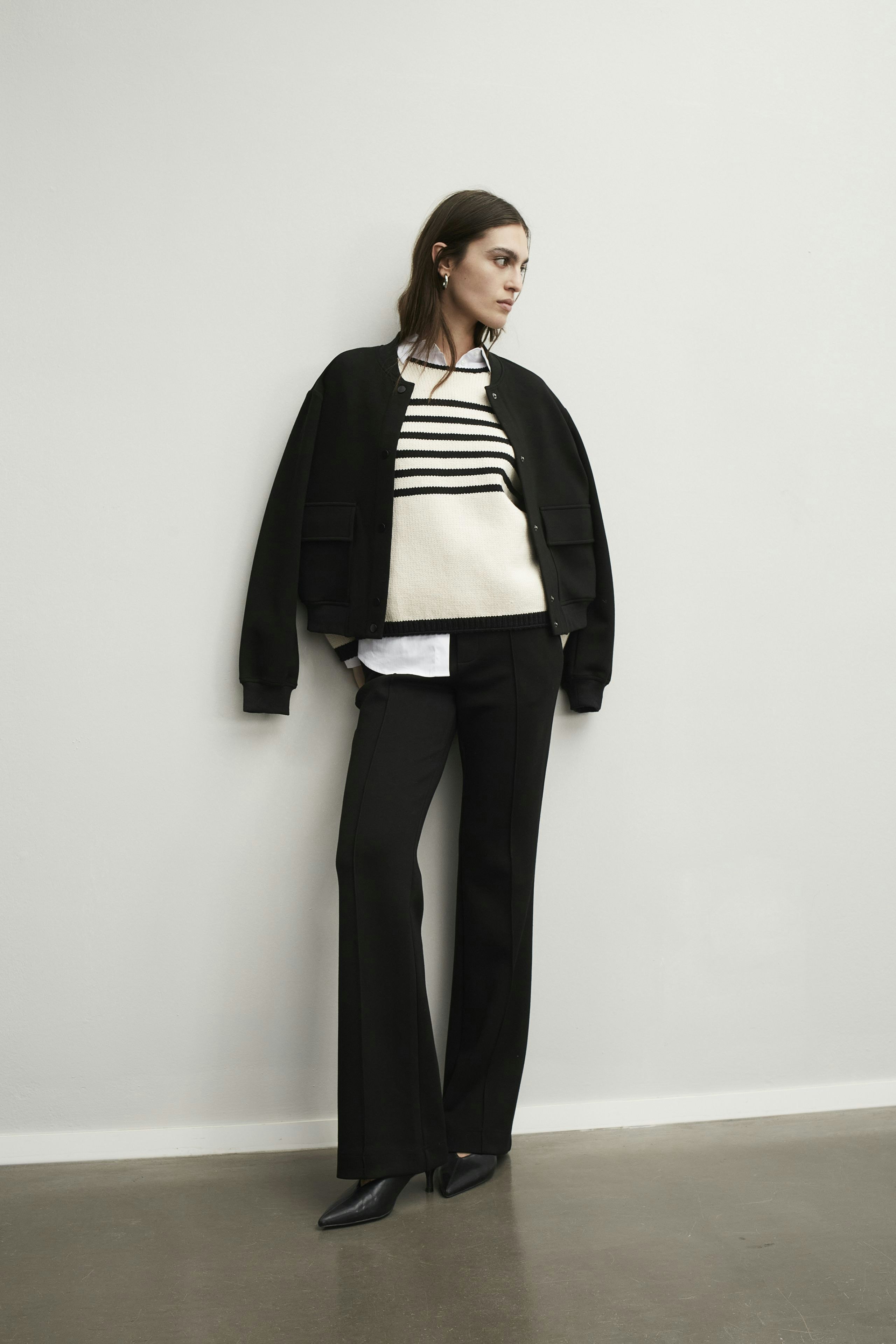 Elegante Damen-Hose: Frau in schwarzer Hose kombiniert mit einem gestreiften Pullover und Bomberjacke.