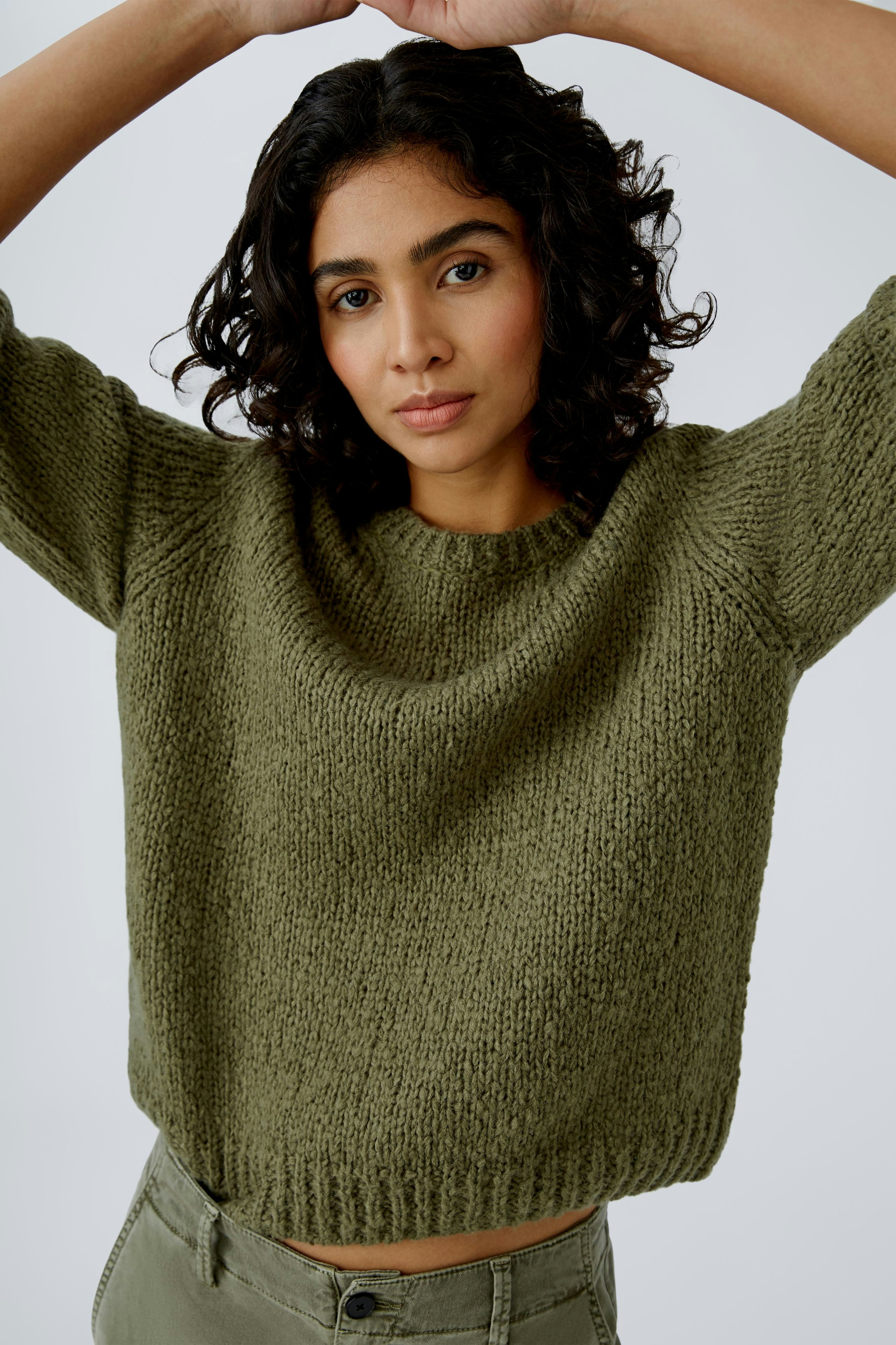 Modern women's pullover: A woman in a cozy olive green knitted pullover, exuding effortless style.