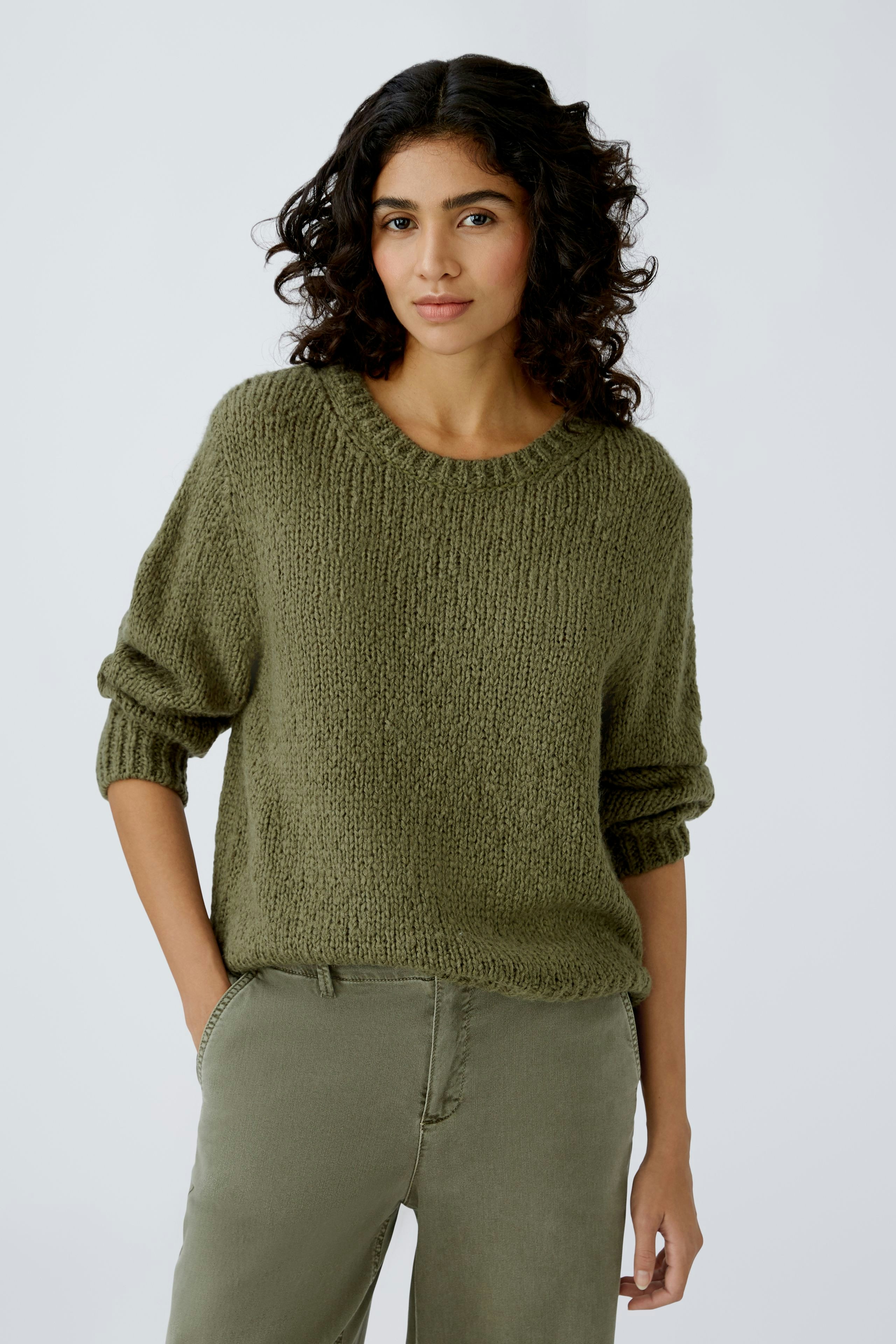 Stylish women's pullover: A woman in a cozy olive green pullover with rolled sleeves.