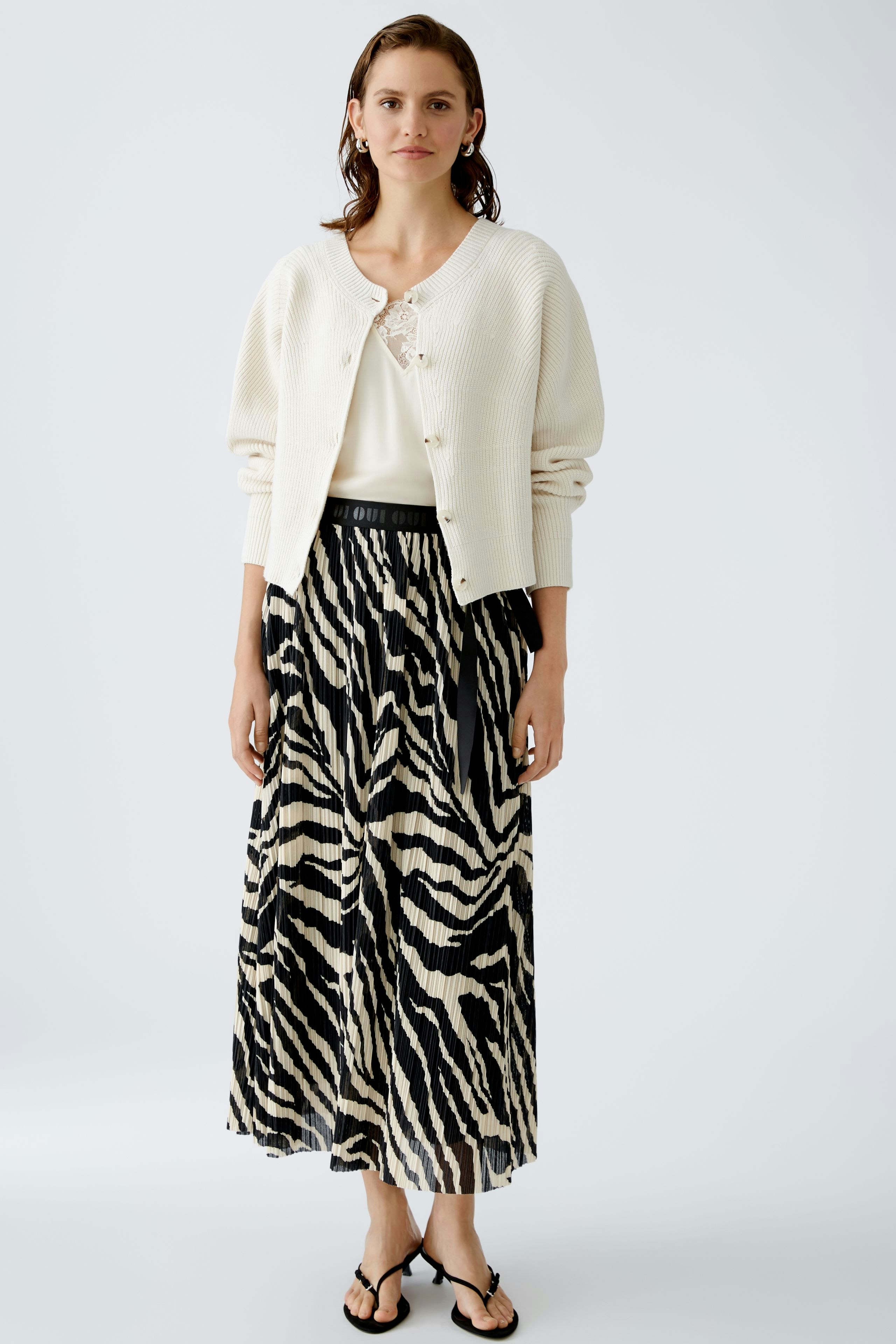 Stylish women's cardigan: A woman in a cream cardigan over a white top, paired with a striped skirt.