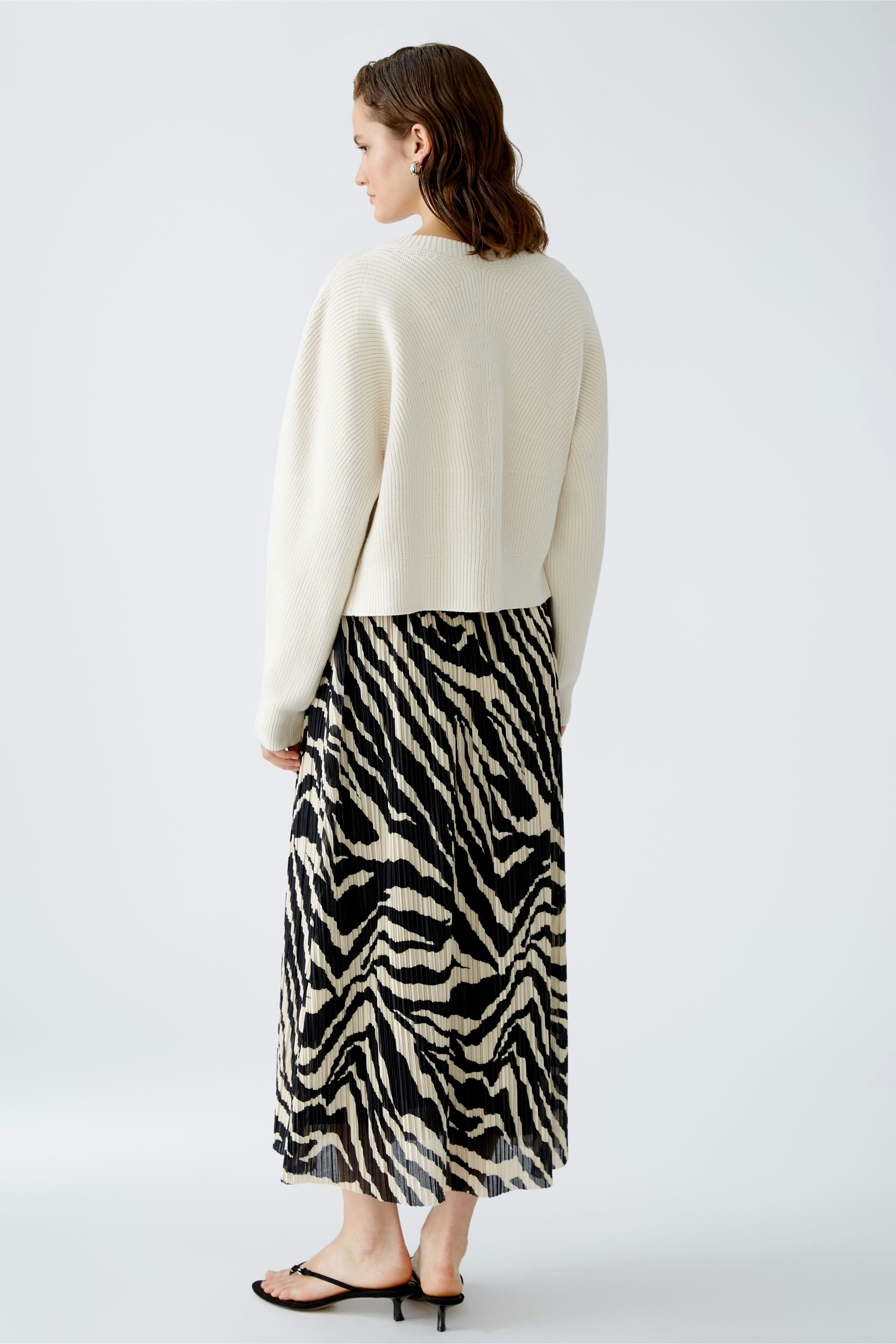 Stylish women's cardigan: A woman in a cream cardigan paired with a flowing zebra-print skirt.