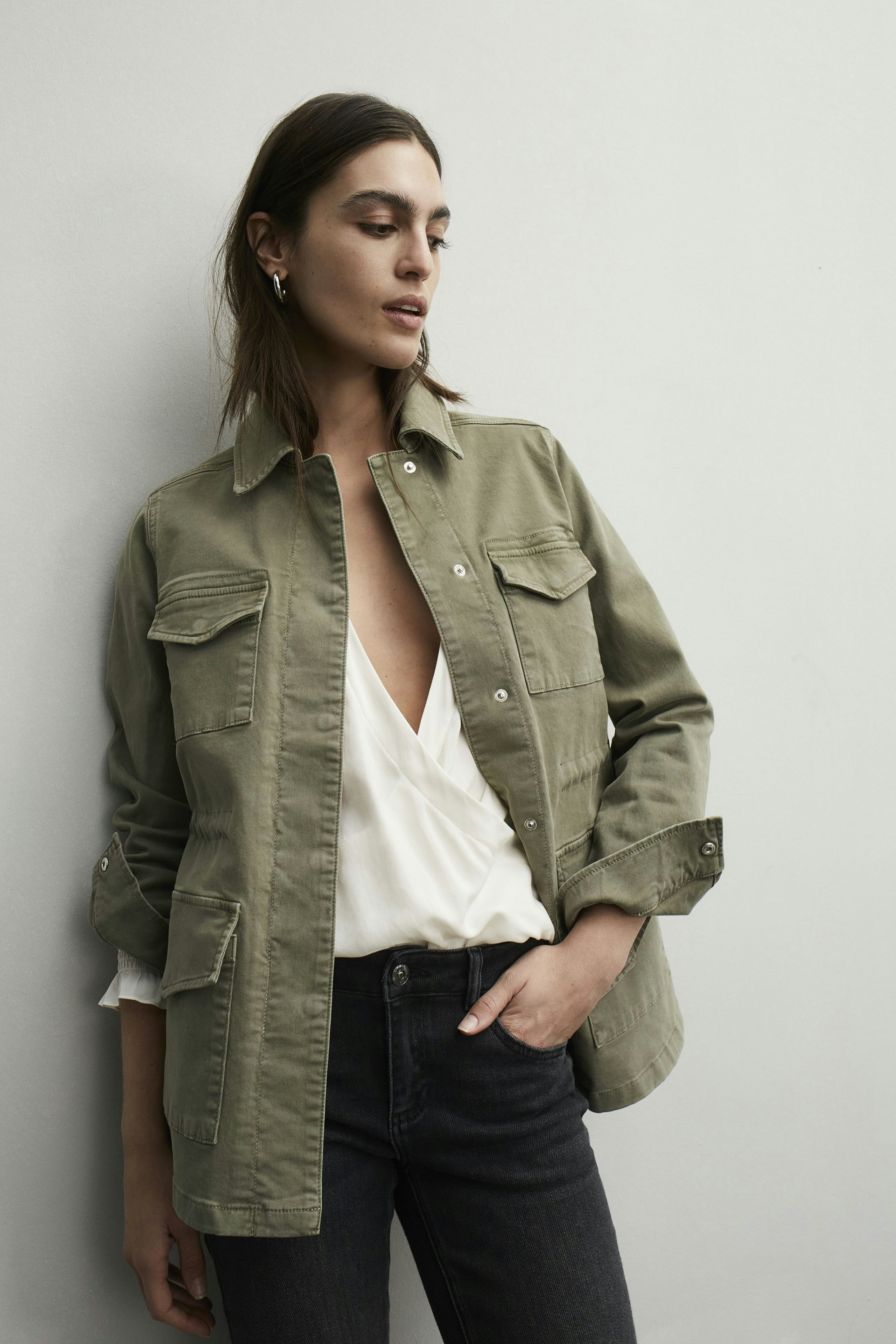 Stylish women's field jacket: A woman in an olive green jacket with pockets, paired with a white top.