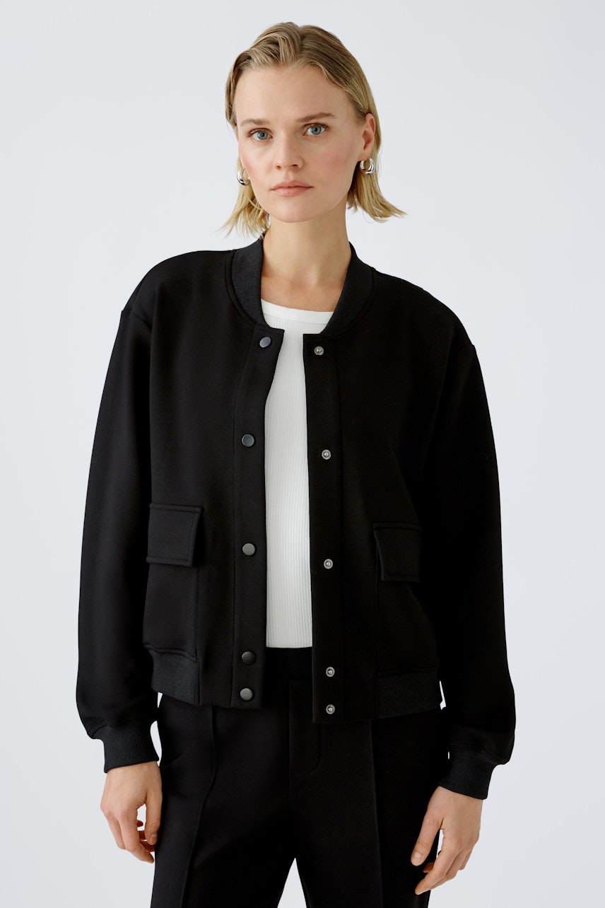 Stylish women's blouson: A woman in a black bomber jacket with pockets, paired with a white top.