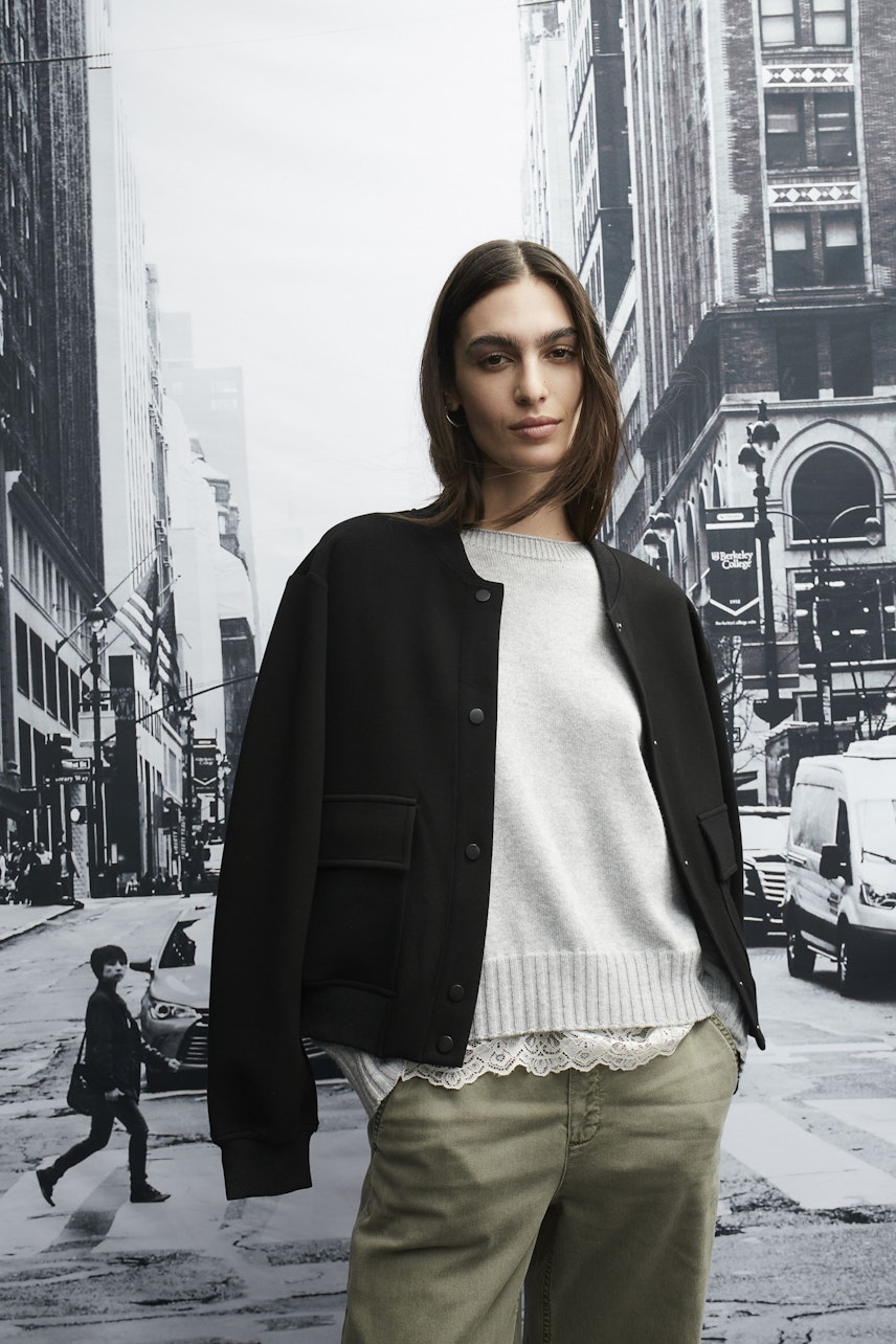 Stylish women's blouson: A woman in a black bomber jacket over a grey pullover, exuding confidence.