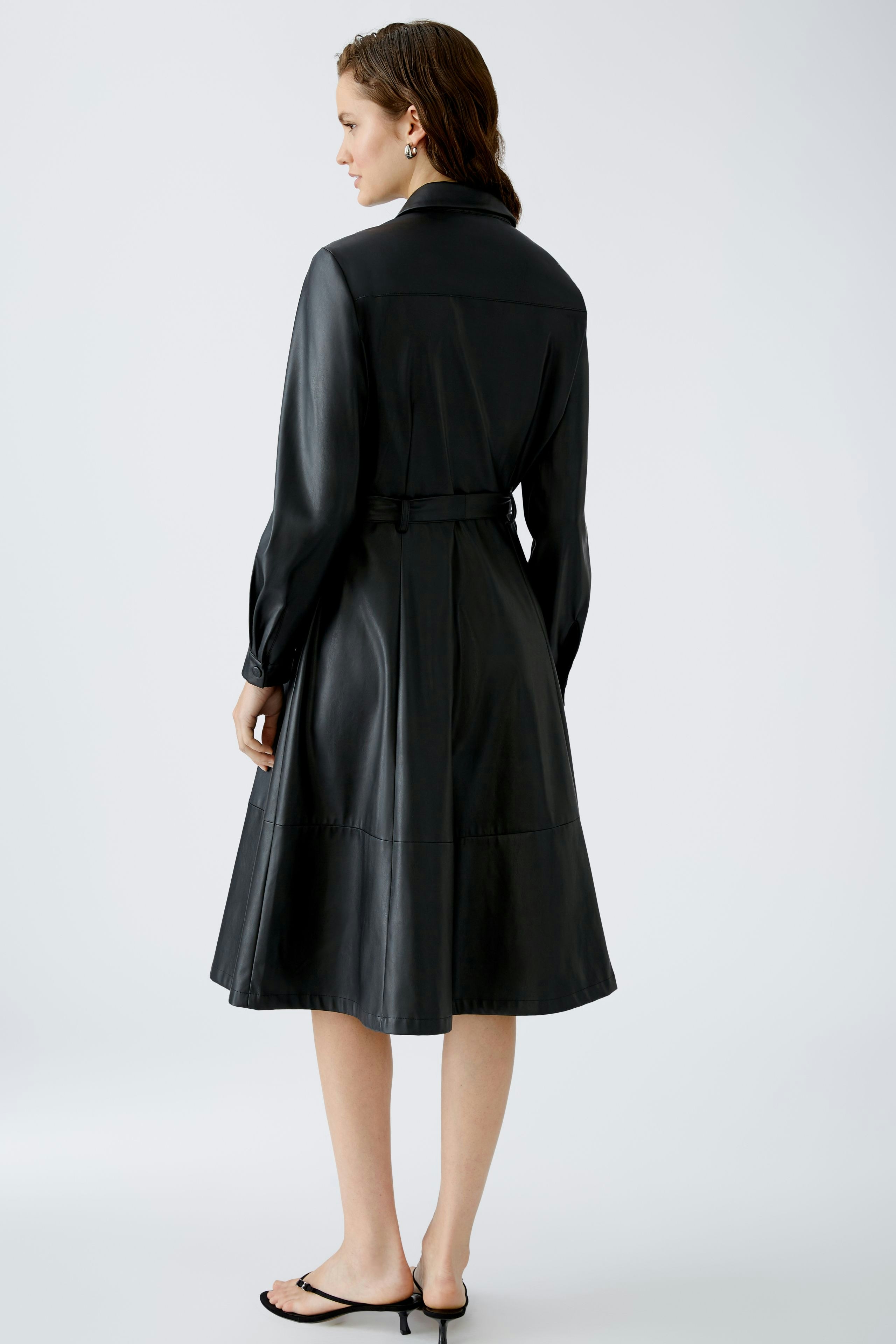 Elegantes Hemdblusenkleid: Frau in schwarzem, tailliertem Kleid mit schickem Kragen und Gürtel.