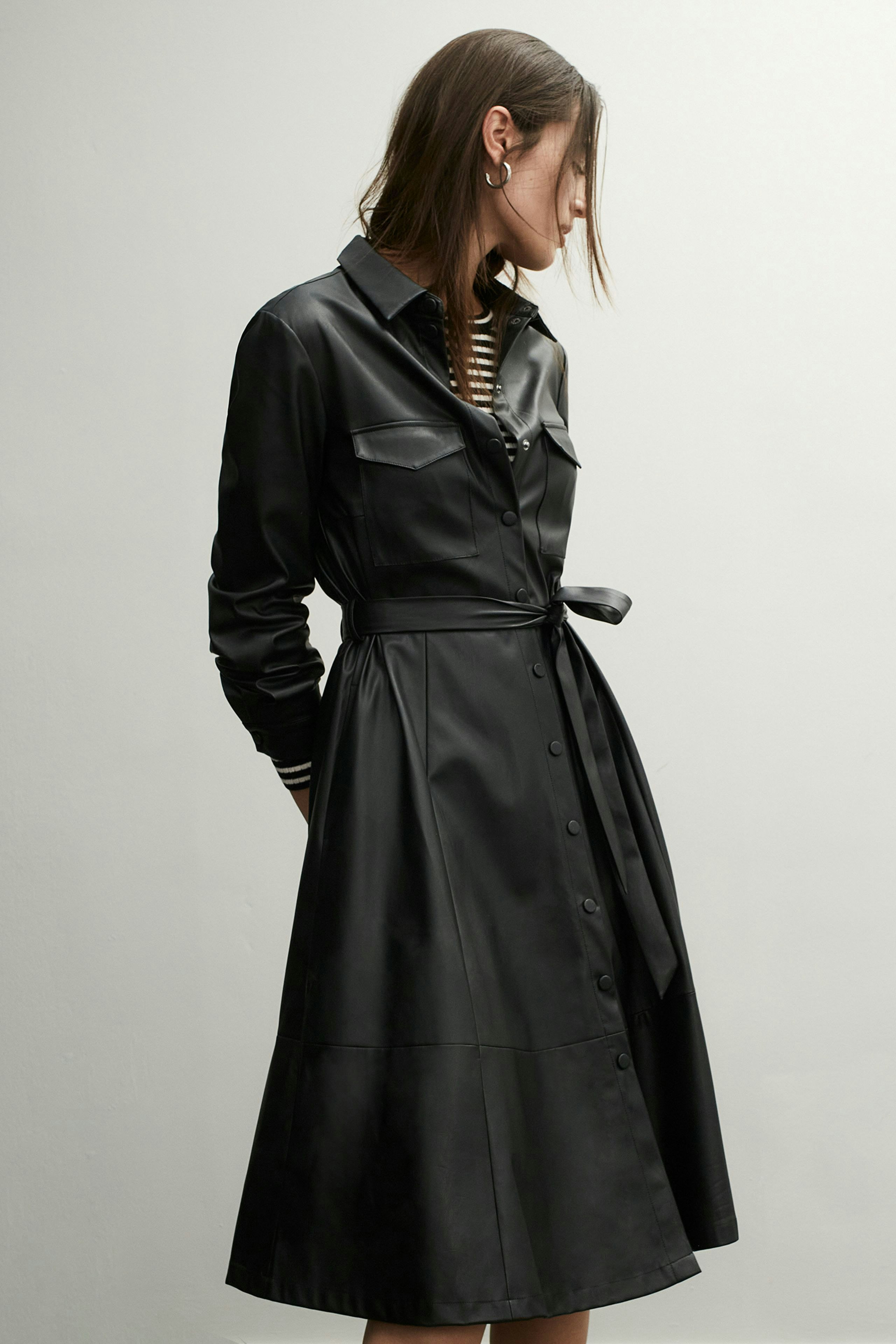 Elegantes Hemdblusenkleid: Frau in schwarzem Lederkleid mit tailliertem Schnitt und Knopfleiste.