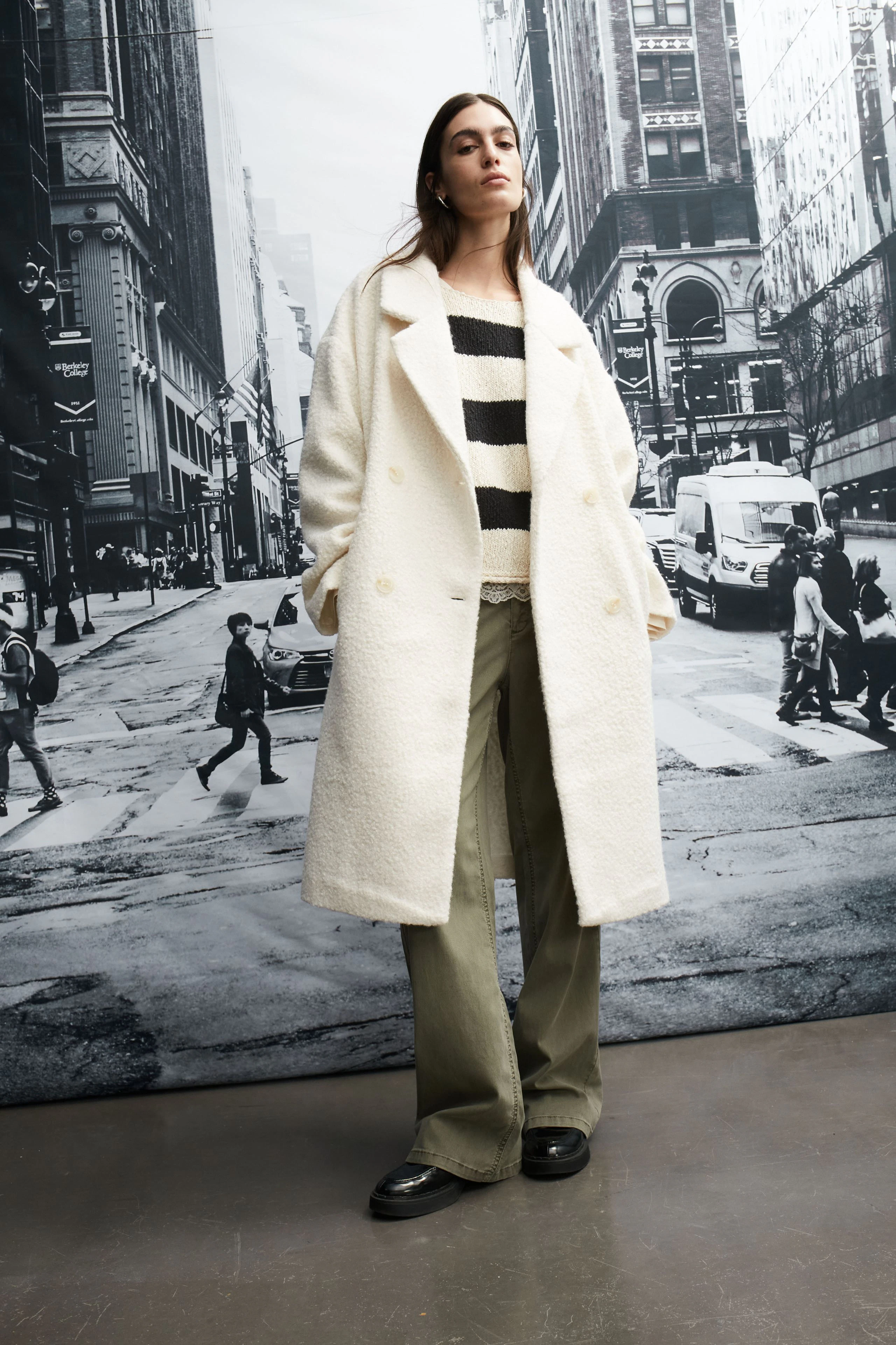 Stylish women's winter coat: A woman in a white coat over a striped pullover and wide pants stands confidently.
