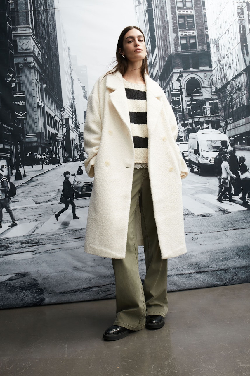 Stylish women's winter coat: A woman in a white coat over a striped pullover and wide pants stands confidently.