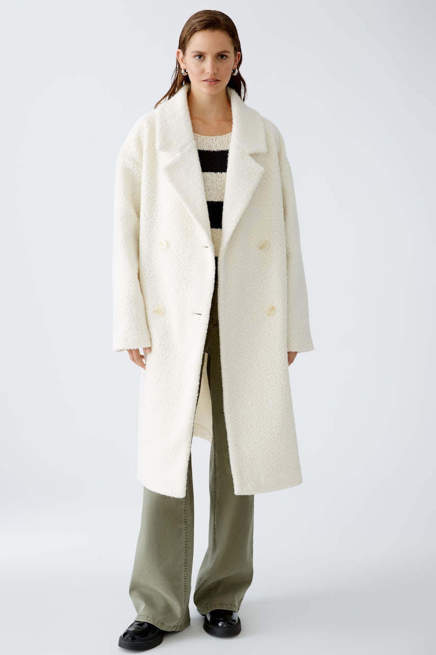 Stylish winter coat: A woman in a cozy white double-breasted coat over a striped pullover and green pants.