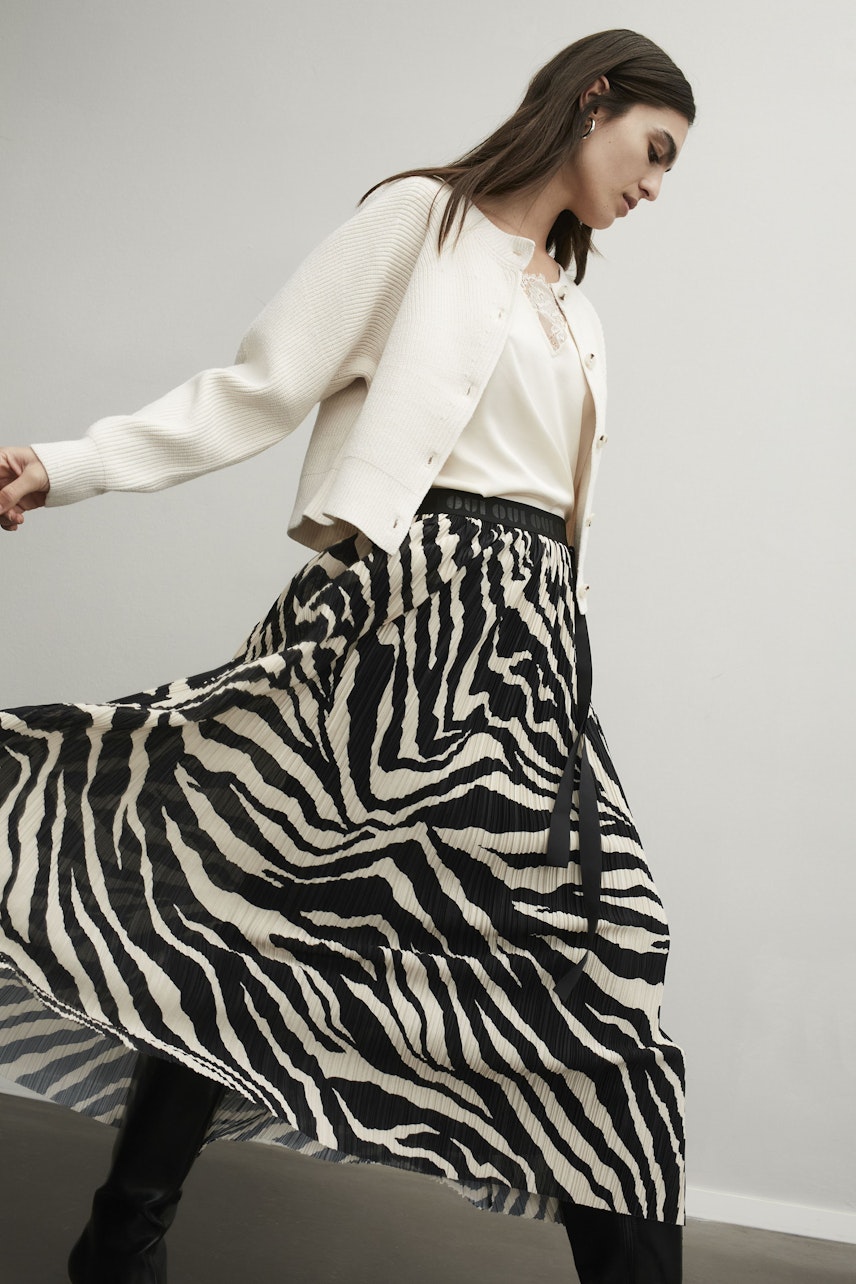 Stylish maxi skirt: Woman in a flowing zebra-patterned skirt, paired with a light cardigan.