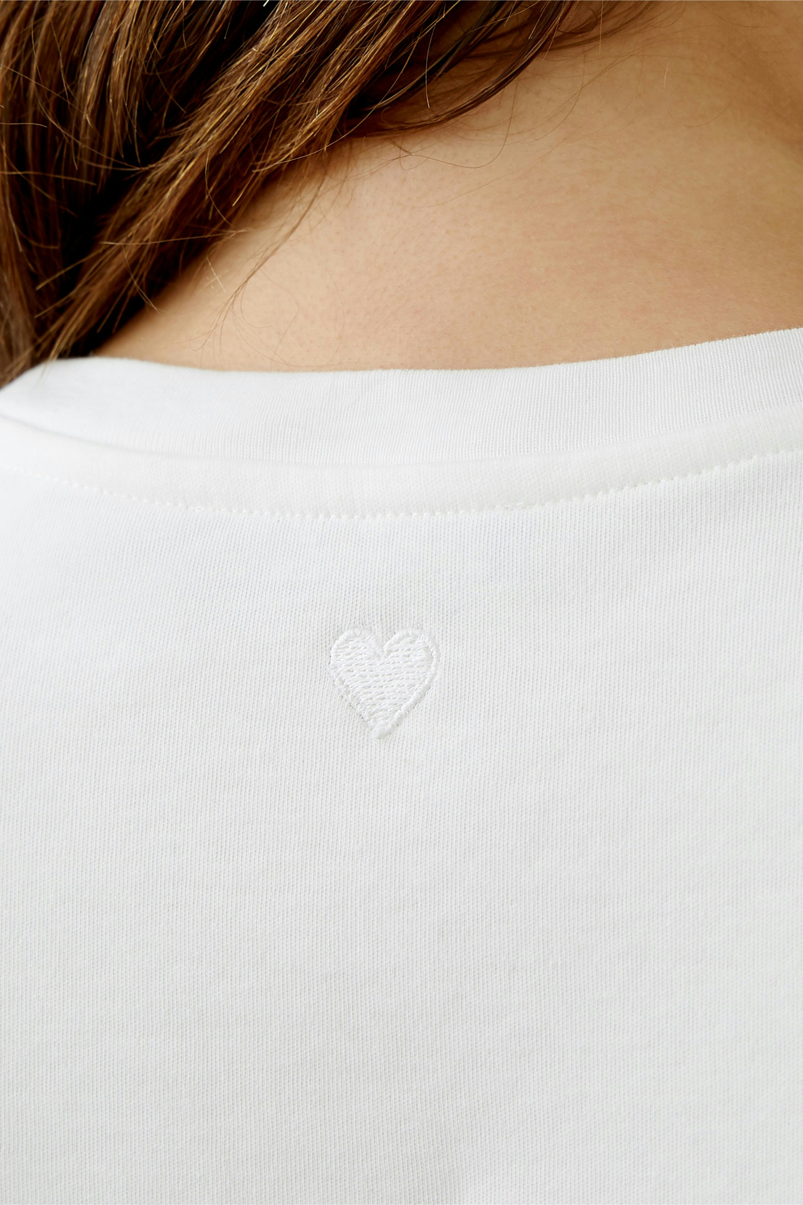 Stylish women's T-shirt: Close-up of a woman wearing a white tee with a heart embroidery on the back.