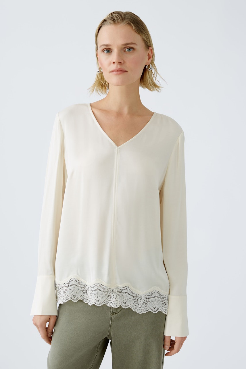 Elegant women's blouse: A woman in a cream blouse with lace trim, styled effortlessly with casual pants.