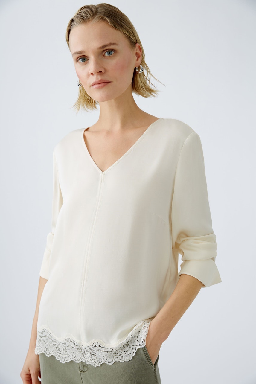 Elegant women's blouse with a V-neck and lace trim, worn by a woman.