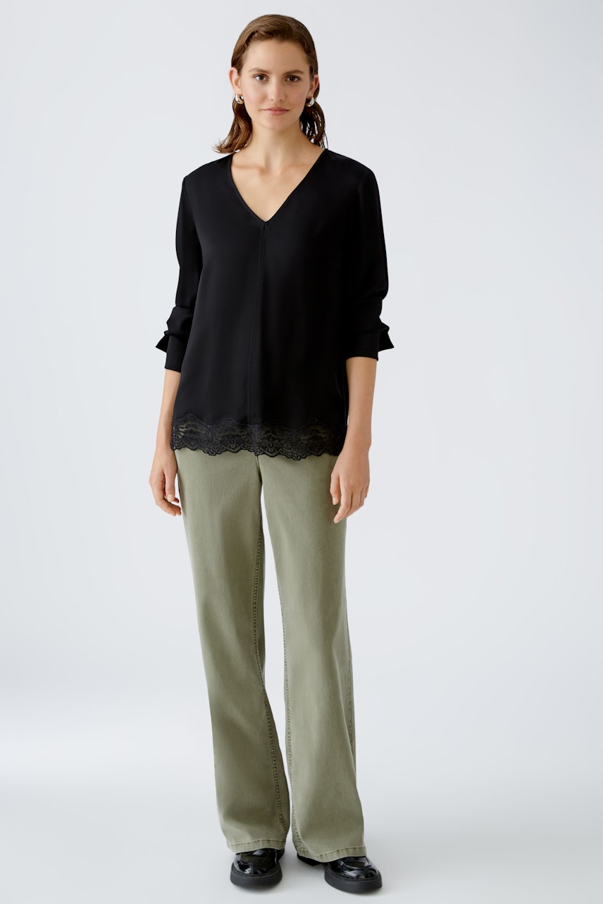 Elegant blouse: A woman in a black blouse with lace trim, paired with relaxed-fit pants.