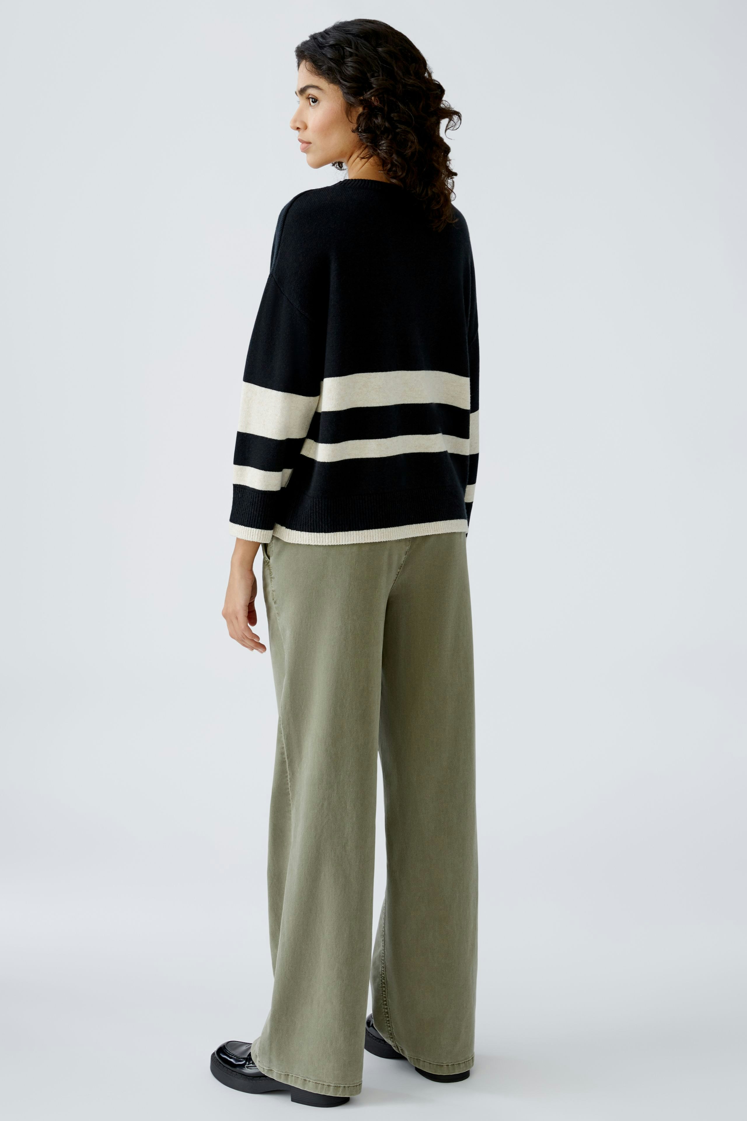 Damen-Pullover: Frau in schwarzem Pullover mit weißen Streifen und lässigen Hosen von hinten.