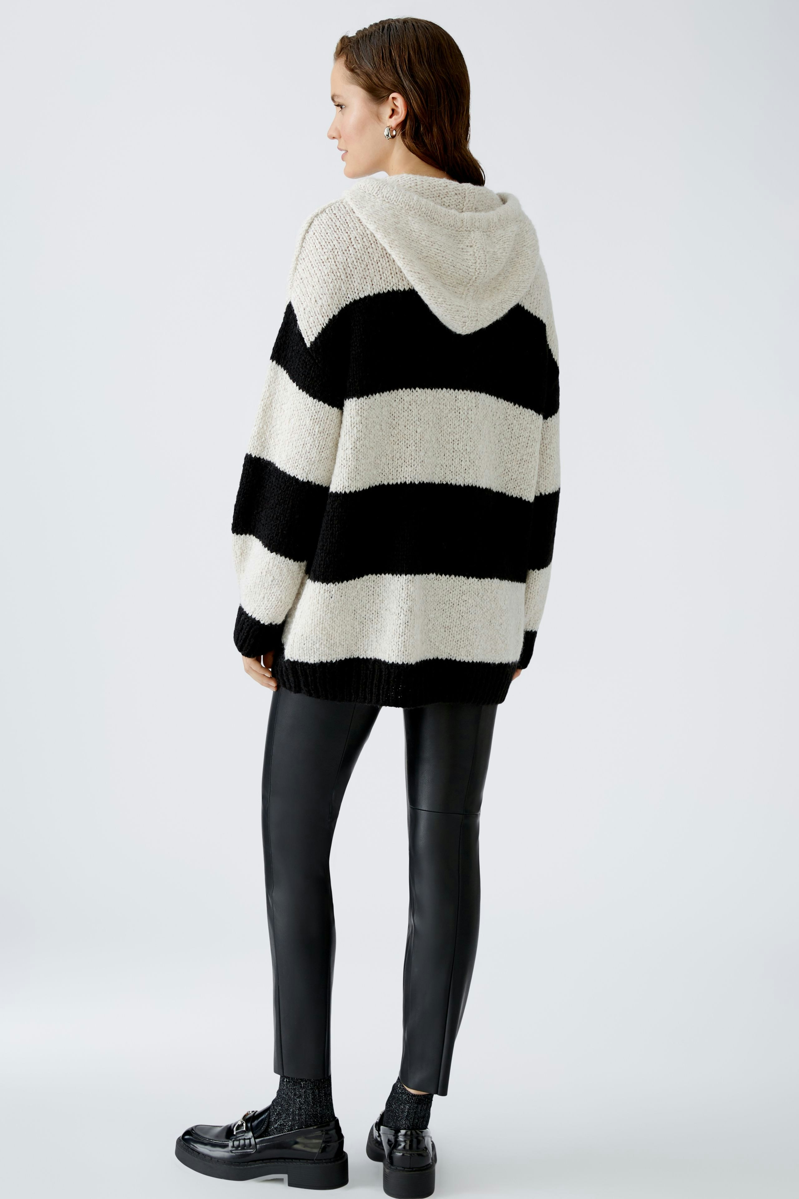 Stylish women's hoodie: A woman in a cozy striped pullover with a hood, paired with sleek black pants.