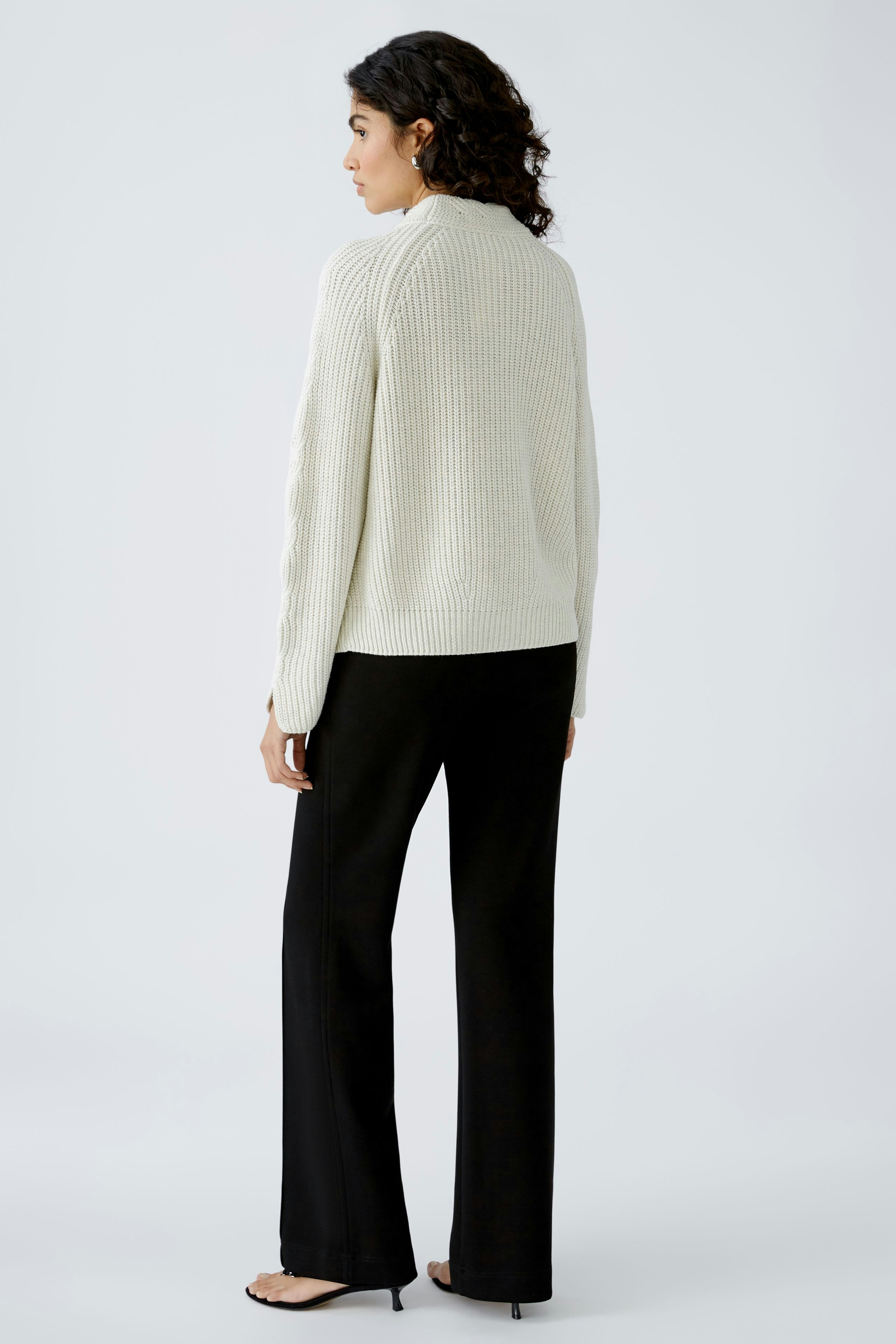 Stylish women's pullover: A woman in a cozy cream pullover, paired with sleek black pants.