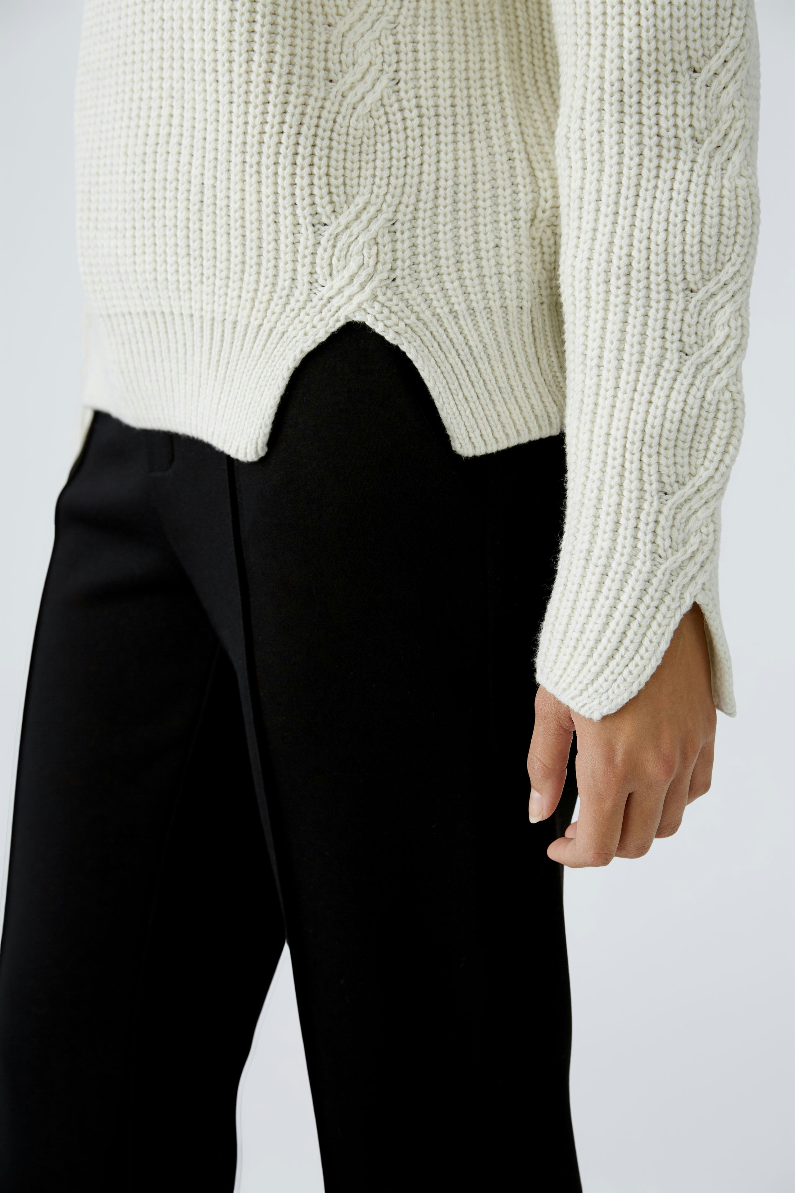 Stylish women's pullover: Close-up of a woman wearing a cream cable-knit pullover with side slits.