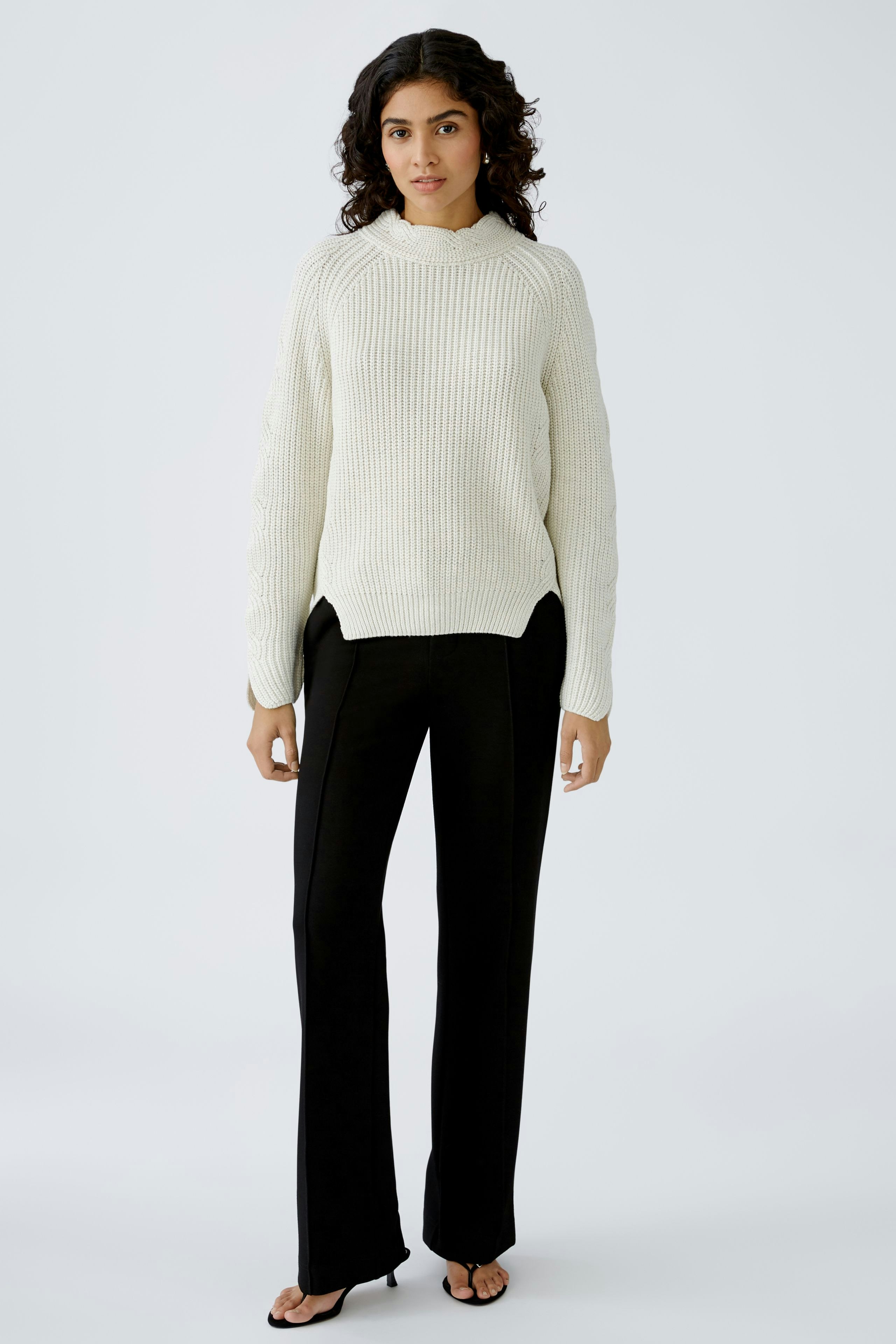 Stylish women's pullover: A woman in a cozy cream pullover paired with sleek black trousers.