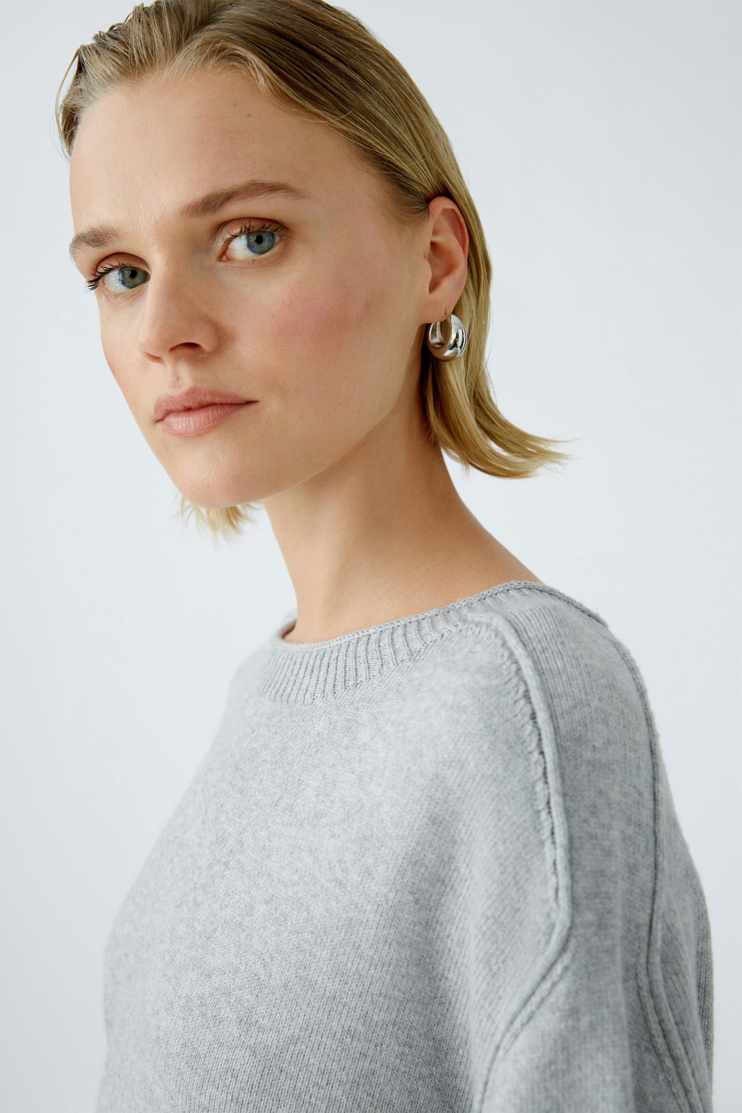 Eleganter Damen-Pullover: Frau mit kurzem, hellgrauem Pullover und lässigem Look.