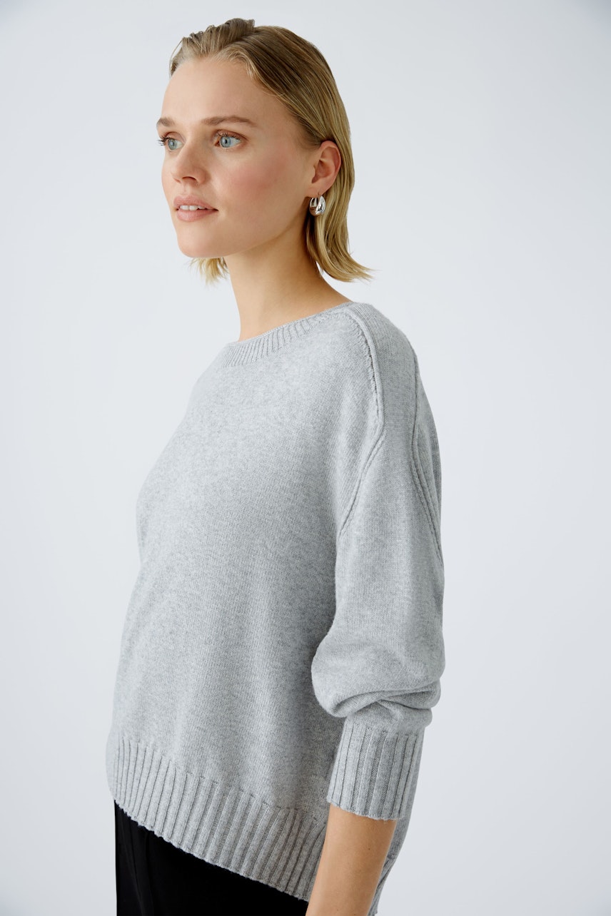 Stylish women's pullover: A woman in a light gray pullover with a relaxed fit and ribbed hem.