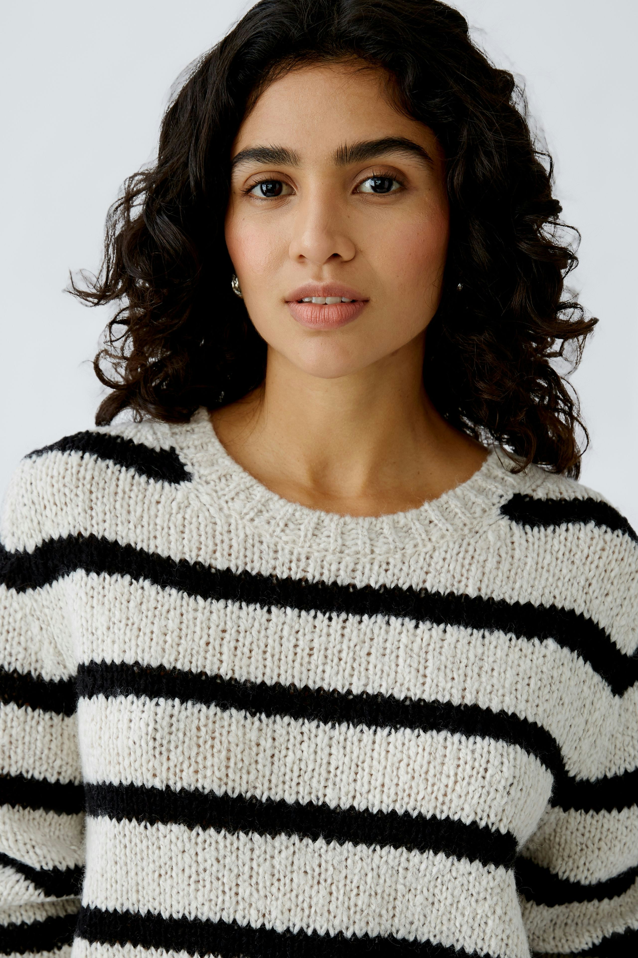 Damen-Pullover: Frau trägt einen gestreiften Pullover in Schwarz und Creme, lässig und modern.