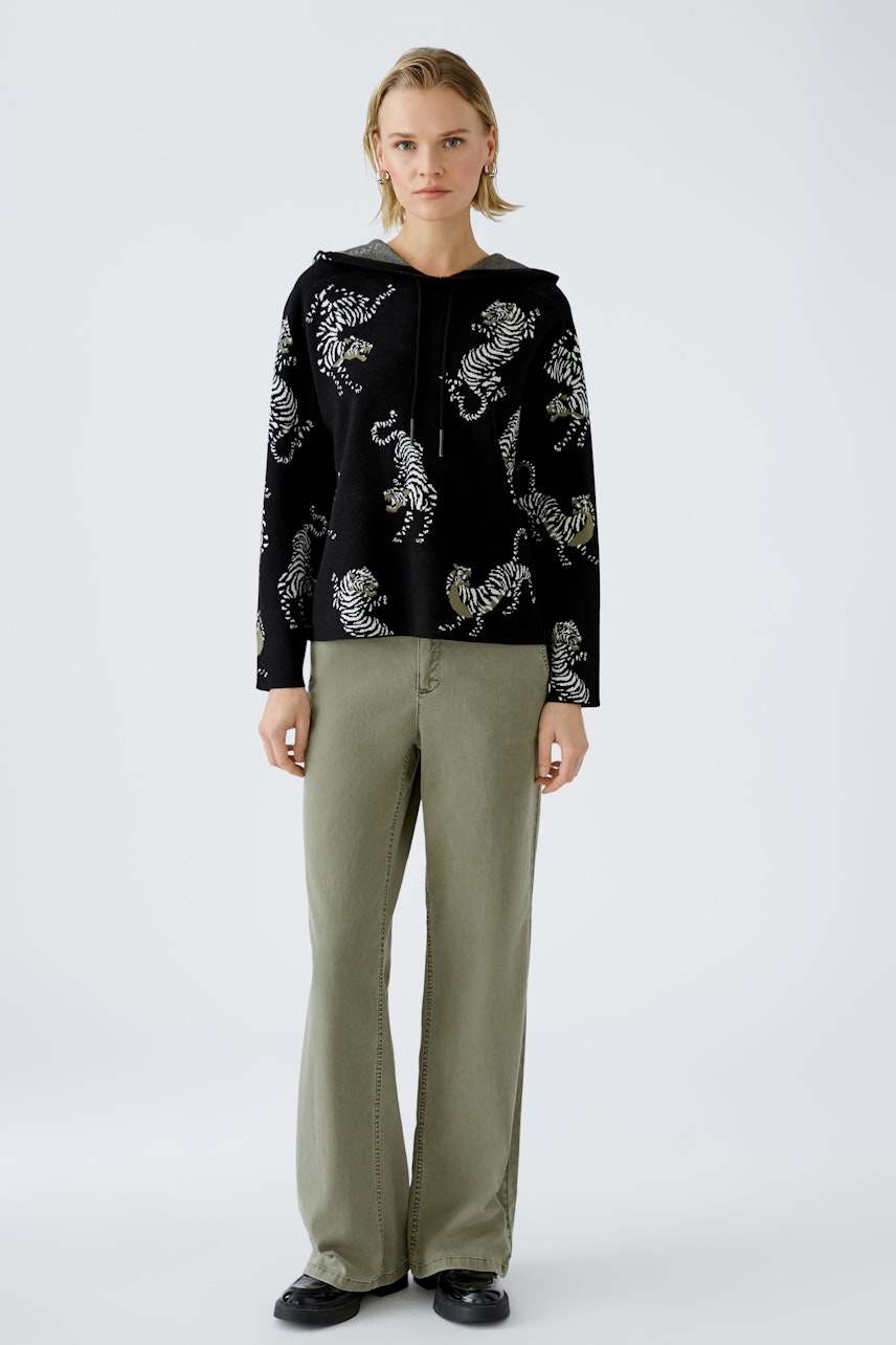 Stylish women's hoodie: A woman in a black pullover with colorful tiger prints, paired with relaxed pants.