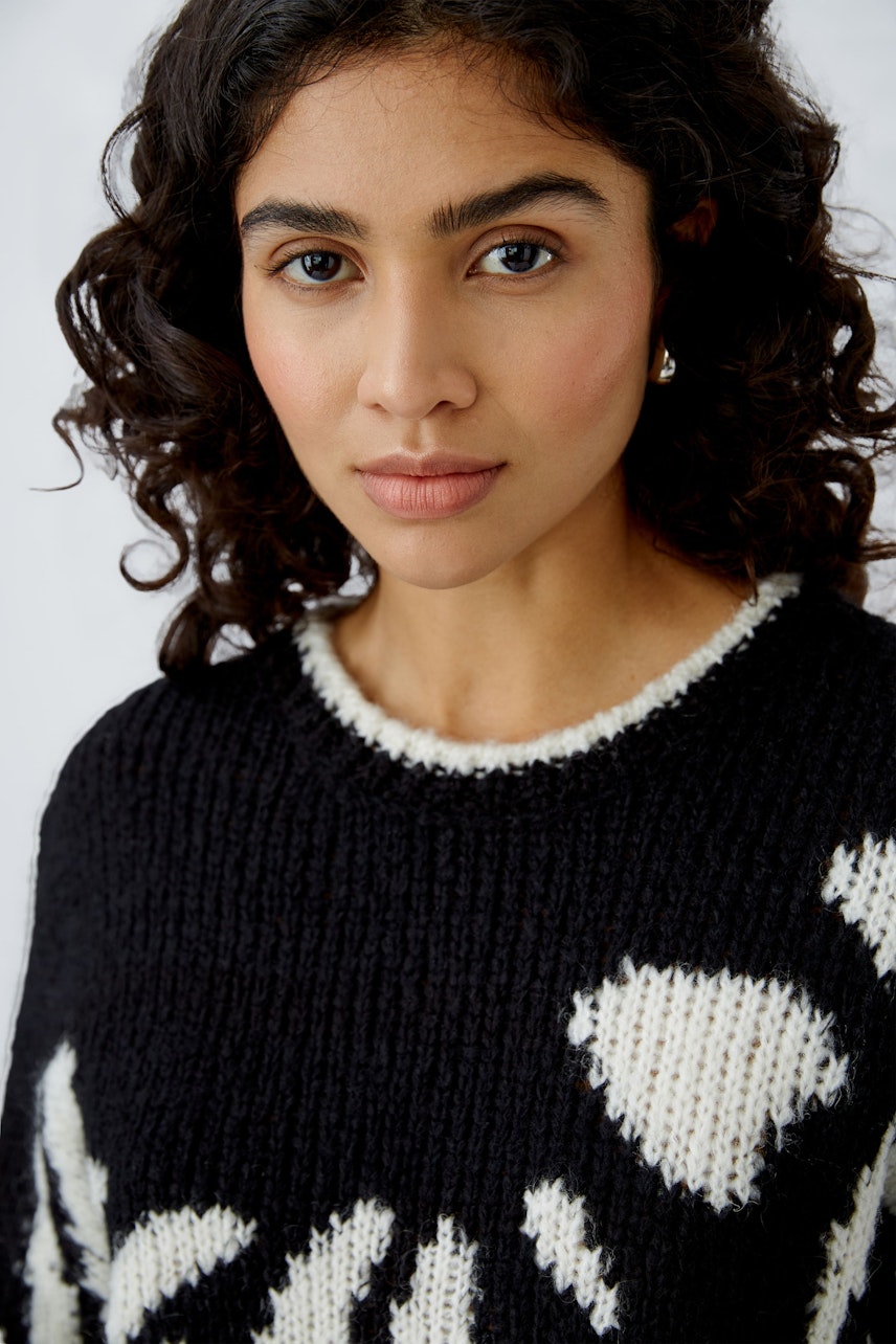 Modern women's pullover: A woman in a black knit pullover with white patterns, exuding confidence.