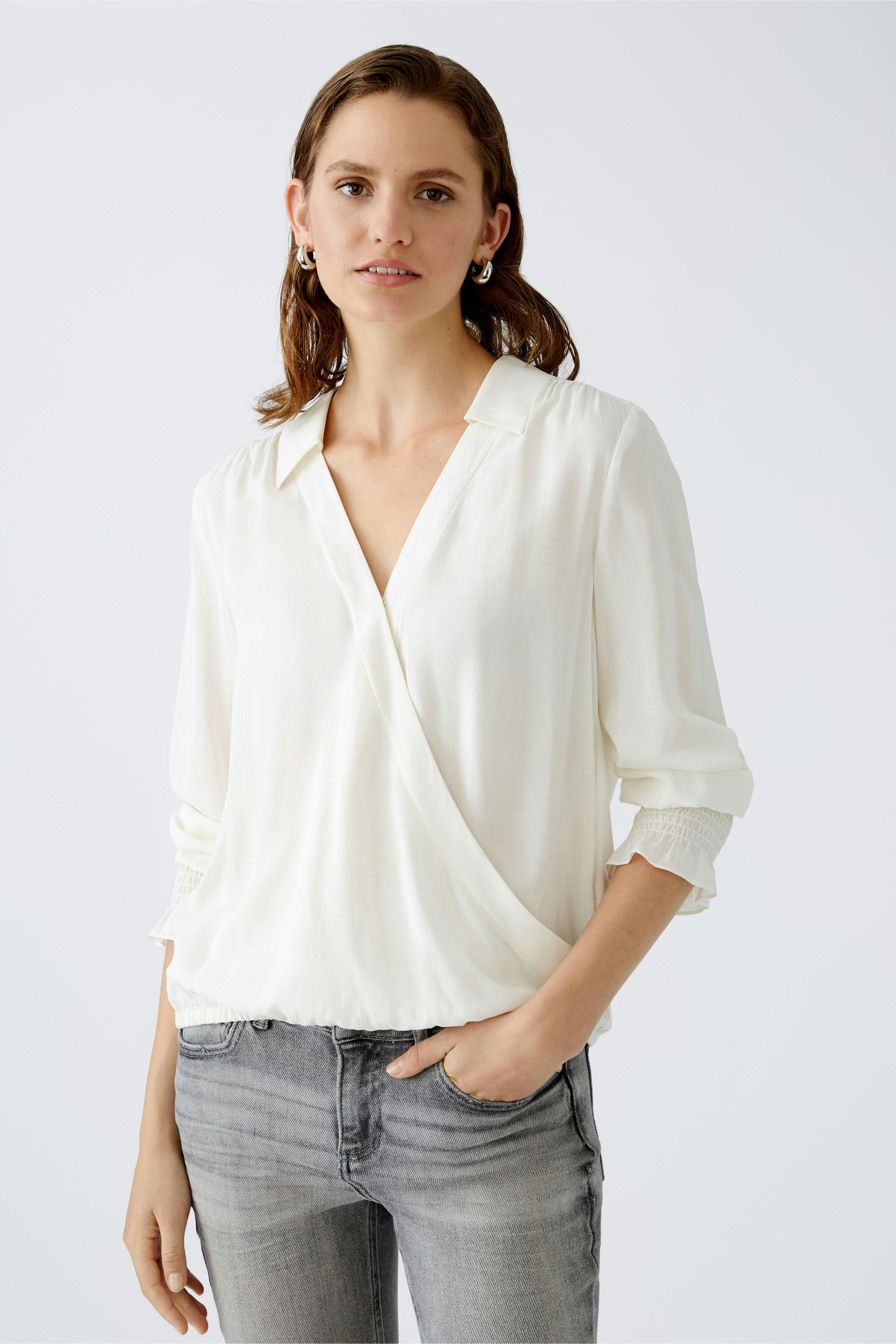 Elegant women's blouse: A woman in a white wrap blouse paired with casual jeans.