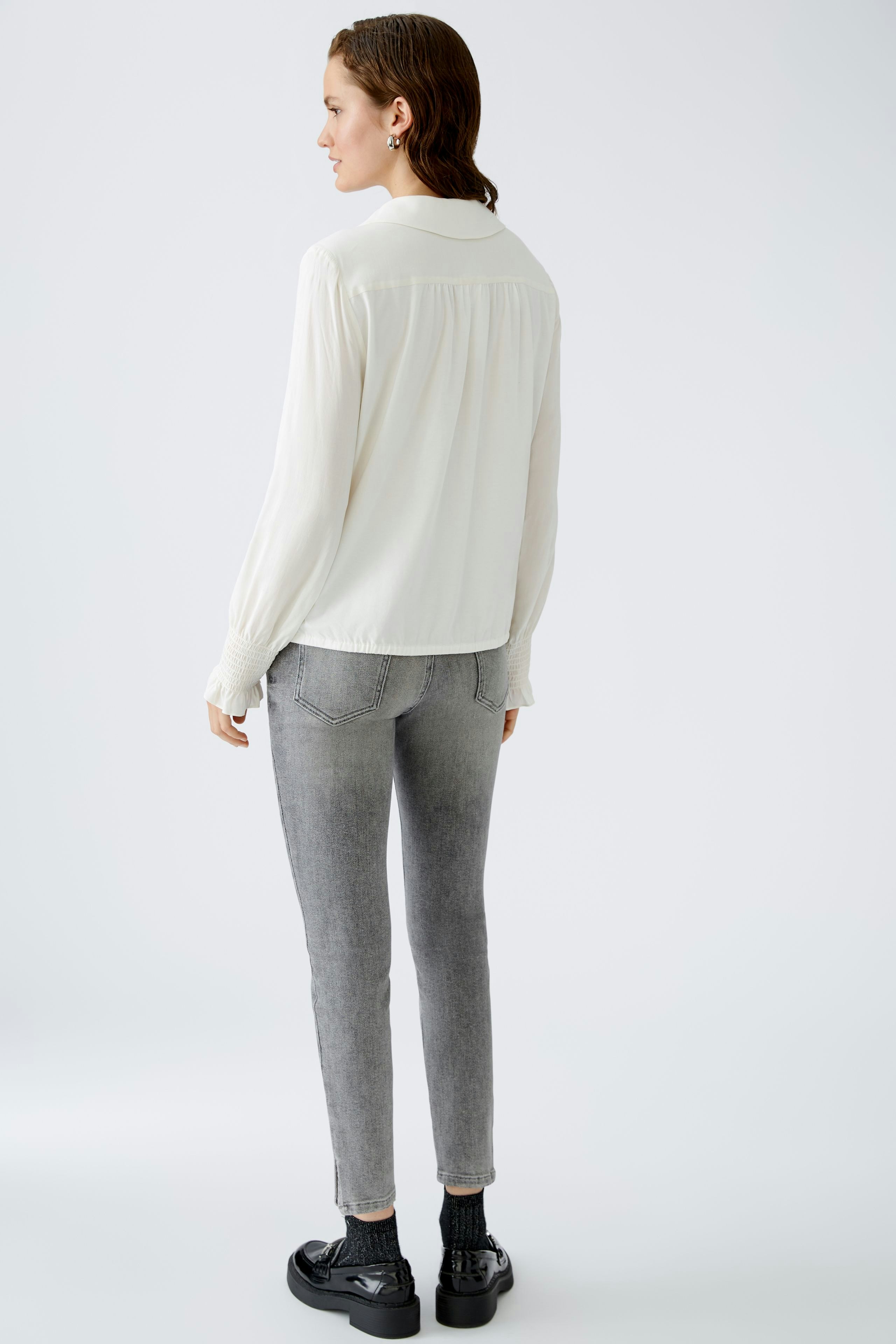 Elegant women's blouse: A woman in a light blouse with a relaxed fit, paired with stylish gray jeans.